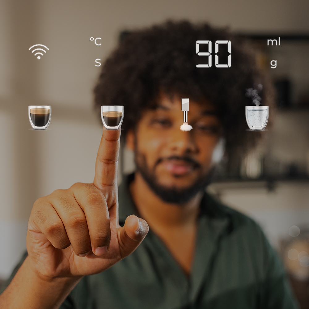 Un hombre señala una interfaz de cafetera inteligente. La pantalla muestra tazas de café, señal WiFi y temperatura. Fondo borroso.