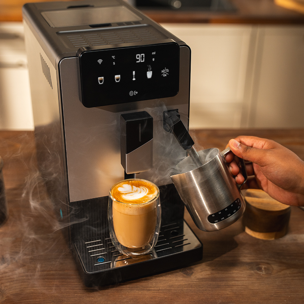 Máquina de café preparando café con leche. Sale vapor. Mano vertiendo leche en un vaso con café. Mesa de madera al frente.