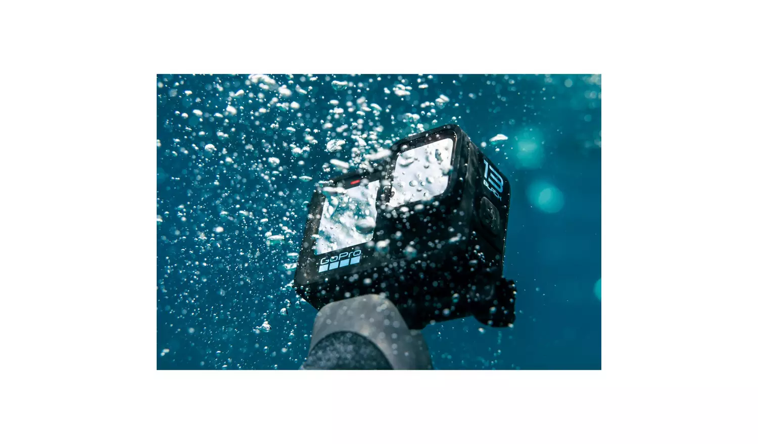 A black GoPro camera submerged underwater, held by a gloved hand. Bubbles surround the camera against a blue background.