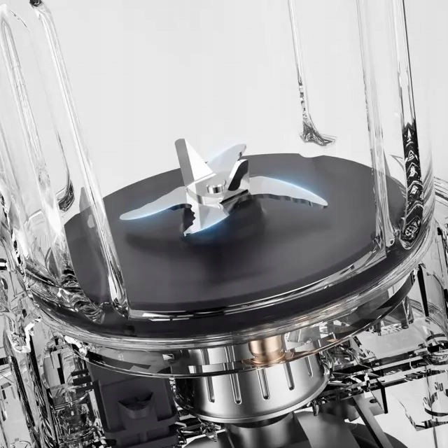 Zbliżenie wnętrza blendera. Ostrza są widoczne, odbijają światło. Szklany pojemnik otacza mechanizm.