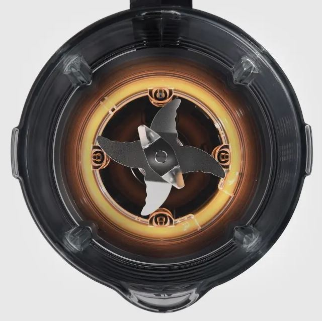 Wnętrze blendera. Ostrza na środku, otoczone żółtym pierścieniem i przezroczystym plastikowym pojemnikiem z czarnymi plastikowymi krawędziami.