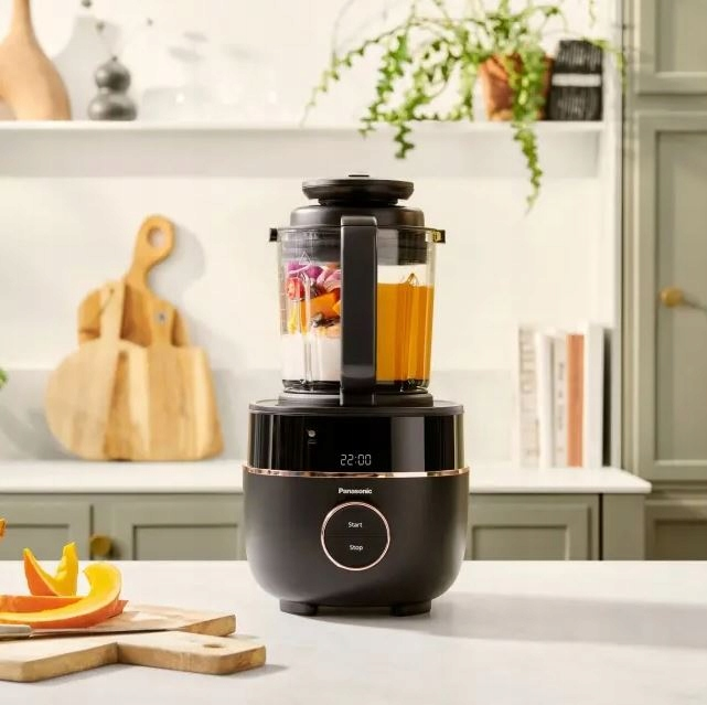 Czarny blender Panasonic z zawartością i blatem. Deska do krojenia i plasterki dyni na pierwszym planie.