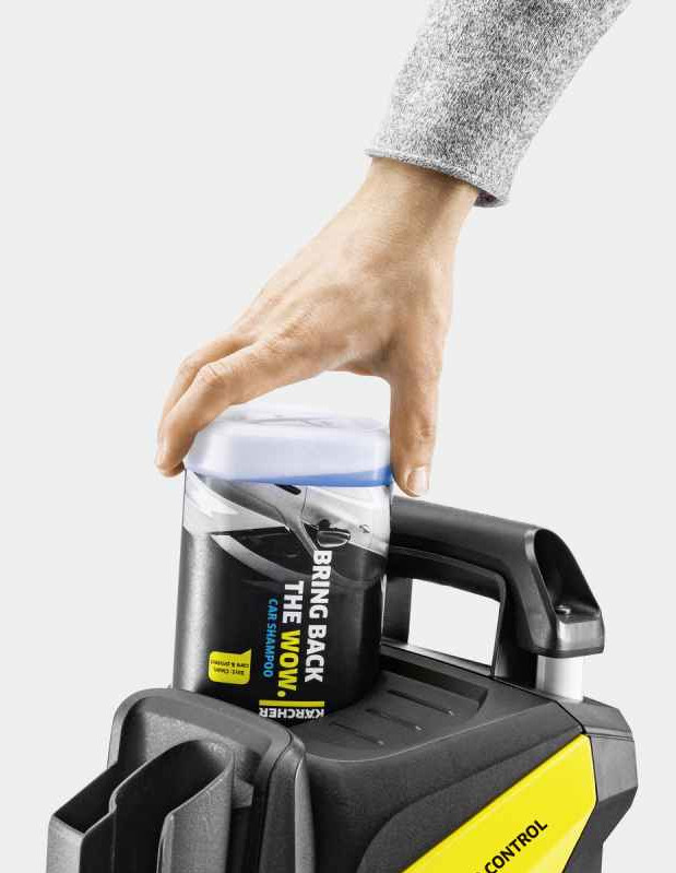 Ręka umieszcza butelkę szamponu samochodowego na czarno-żółtej myjce ciśnieniowej. Butelka jest czarna, z napisem 'Bring back the Wow'.