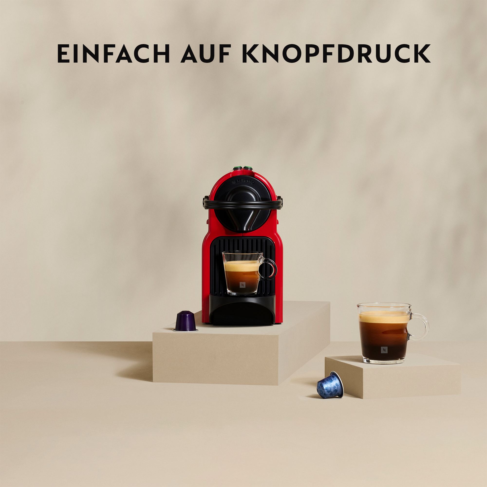 Rote Nespresso-Maschine mit Kaffee in einem Glas, zwei Kaffeekapseln und den Worten 'EINFACH AUF KNOPFDRUCK'.