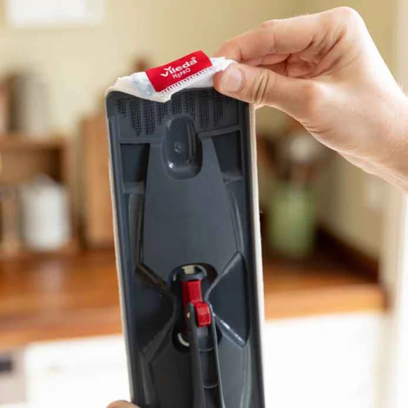 Ręka trzyma głowicę mopa Vileda. Głowica mopa jest szara i biała z czerwoną etykietą. Tło jest rozmyte.