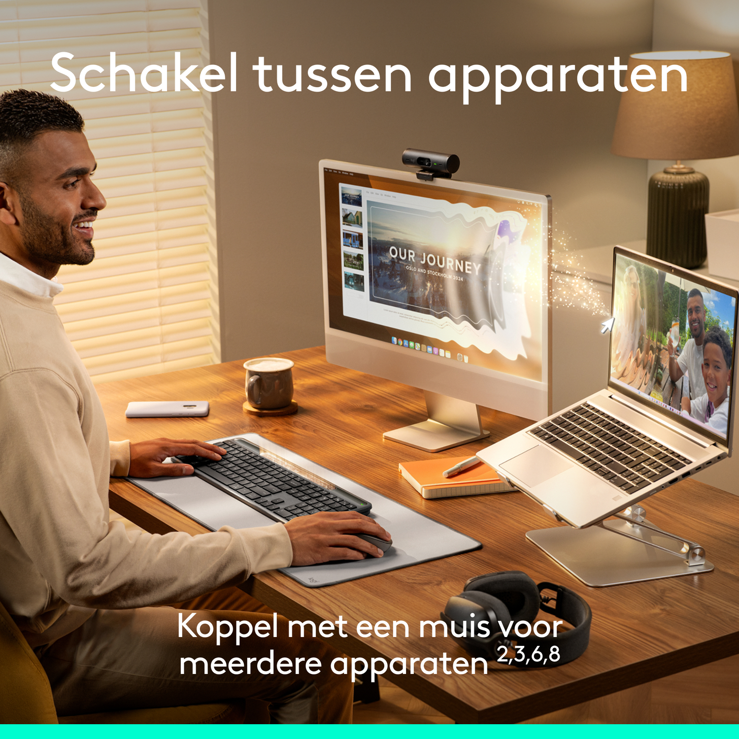 Man using keyboard and mouse with a laptop and monitor. Text on screen reads 'OUR JOURNEY'. Headphones and a lamp are visible.