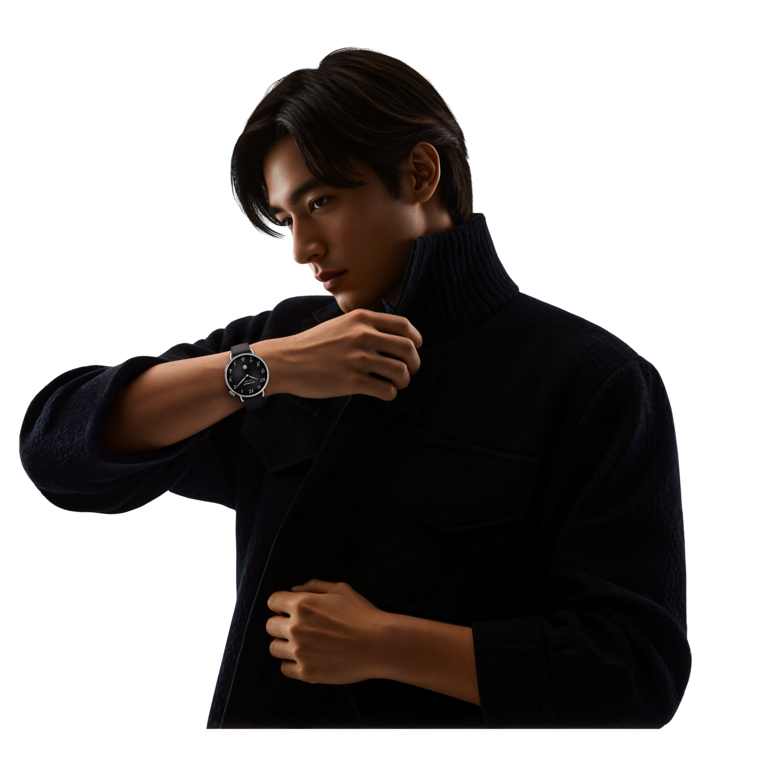 Un homme en veste noire et col roulé regarde une montre à son poignet. La montre a un bracelet noir et un cadran argenté.