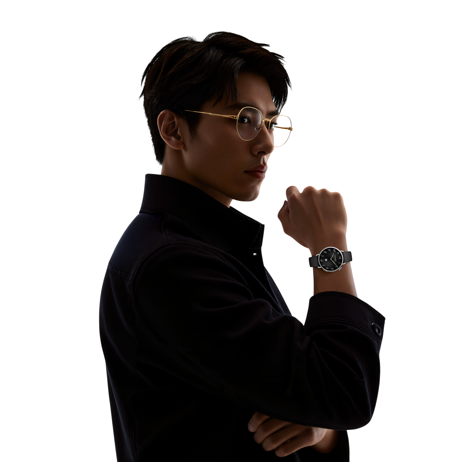 Un homme portant des lunettes et une montre regarde par-dessus son épaule. Il porte une veste noire. Le fond est noir.