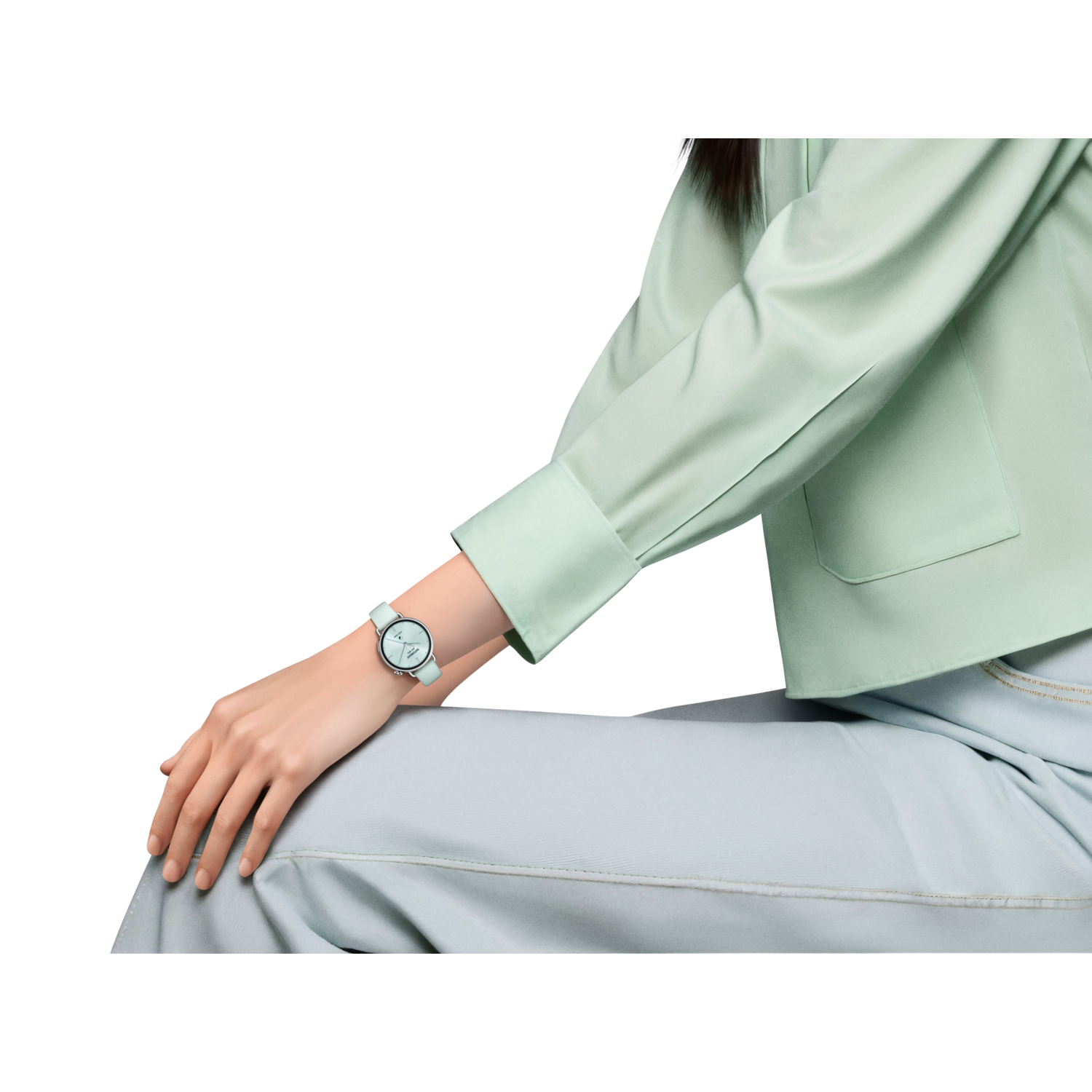 Une personne porte une montre vert menthe. Elle porte une chemise vert menthe et un pantalon bleu clair, sur fond noir.