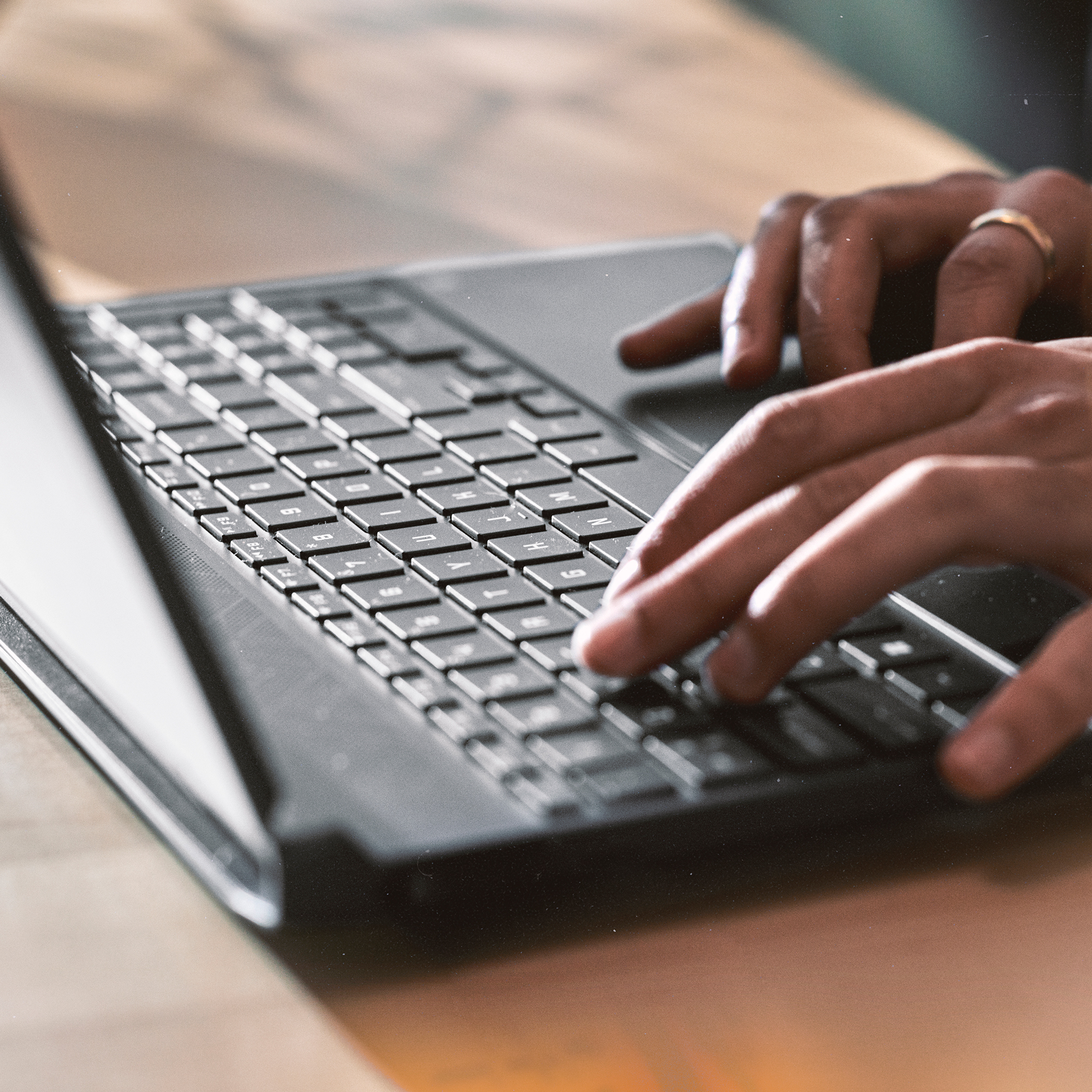 Ręce piszące na klawiaturze laptopa. Tło to drewniany stół.