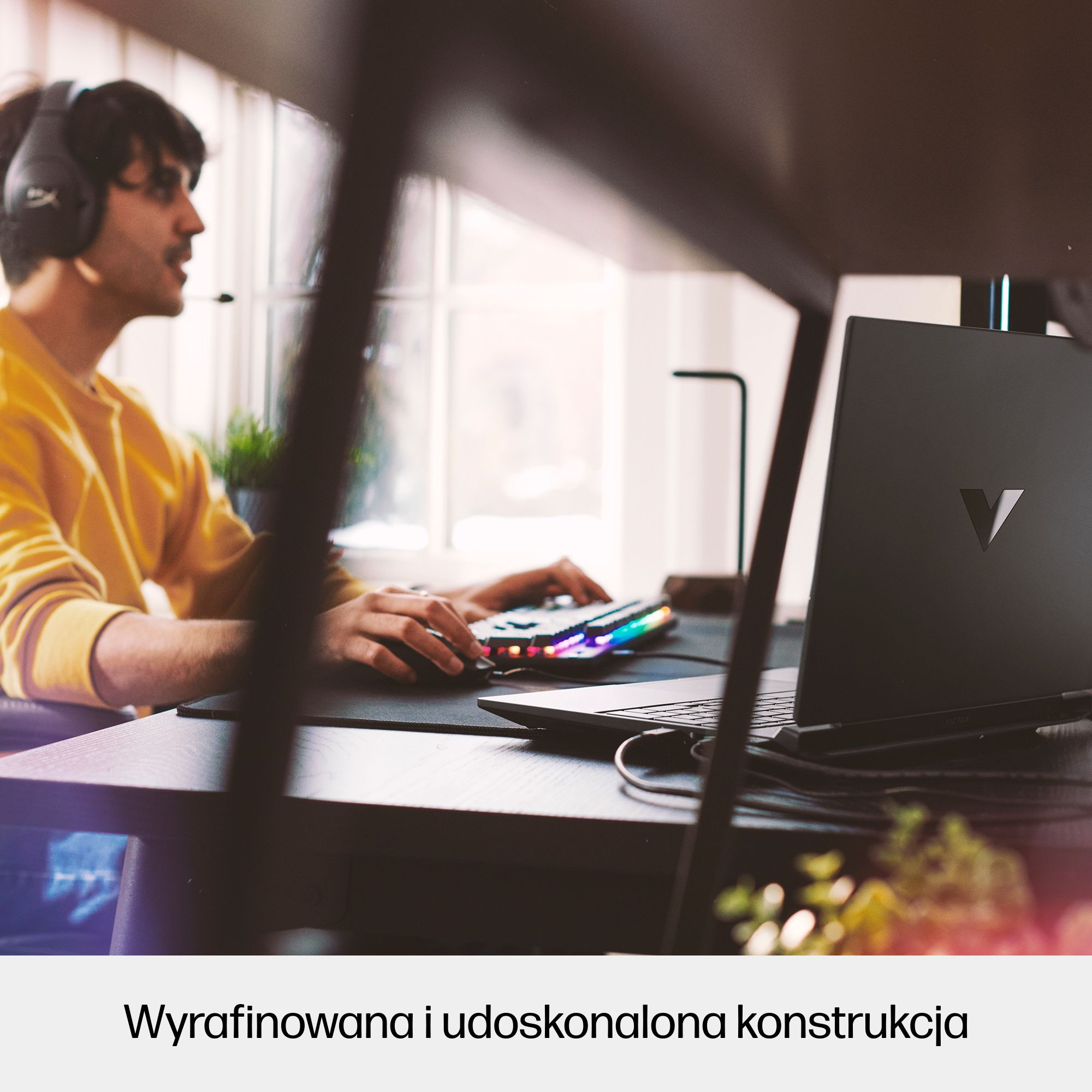 Osoba w słuchawkach gra na laptopie. Widoczna jest kolorowa klawiatura i okno w tle.