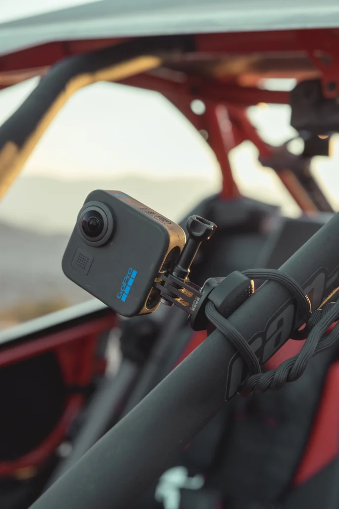 Eine schwarze GoPro-Kamera ist an einer schwarzen Stange befestigt. Die Kamera ist an einer rot-schwarzen Struktur befestigt.