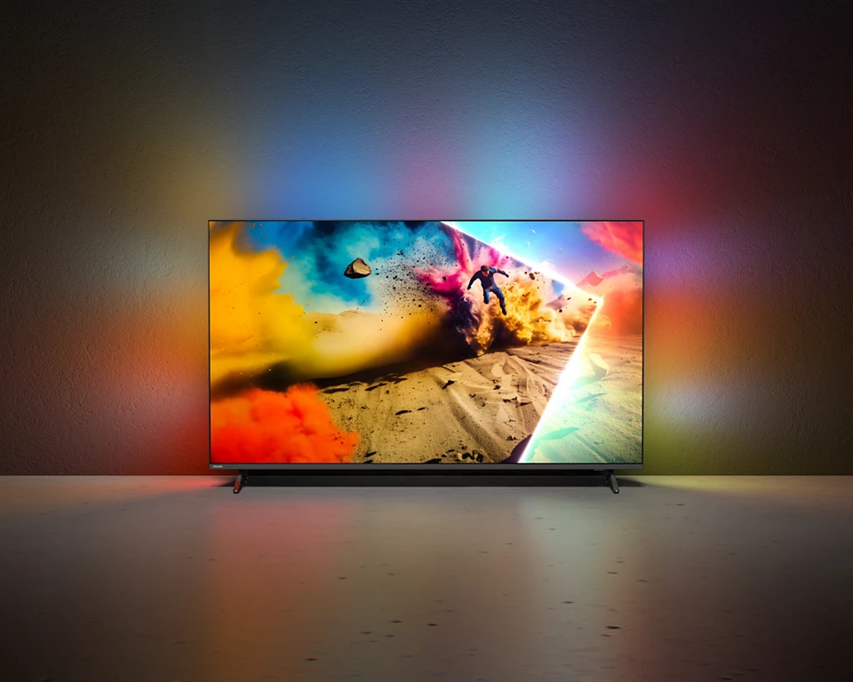 Ein Fernseher zeigt eine bunte Szene einer springenden Person. Die Wand dahinter und der Boden davor sind in leuchtenden Farben beleuchtet.