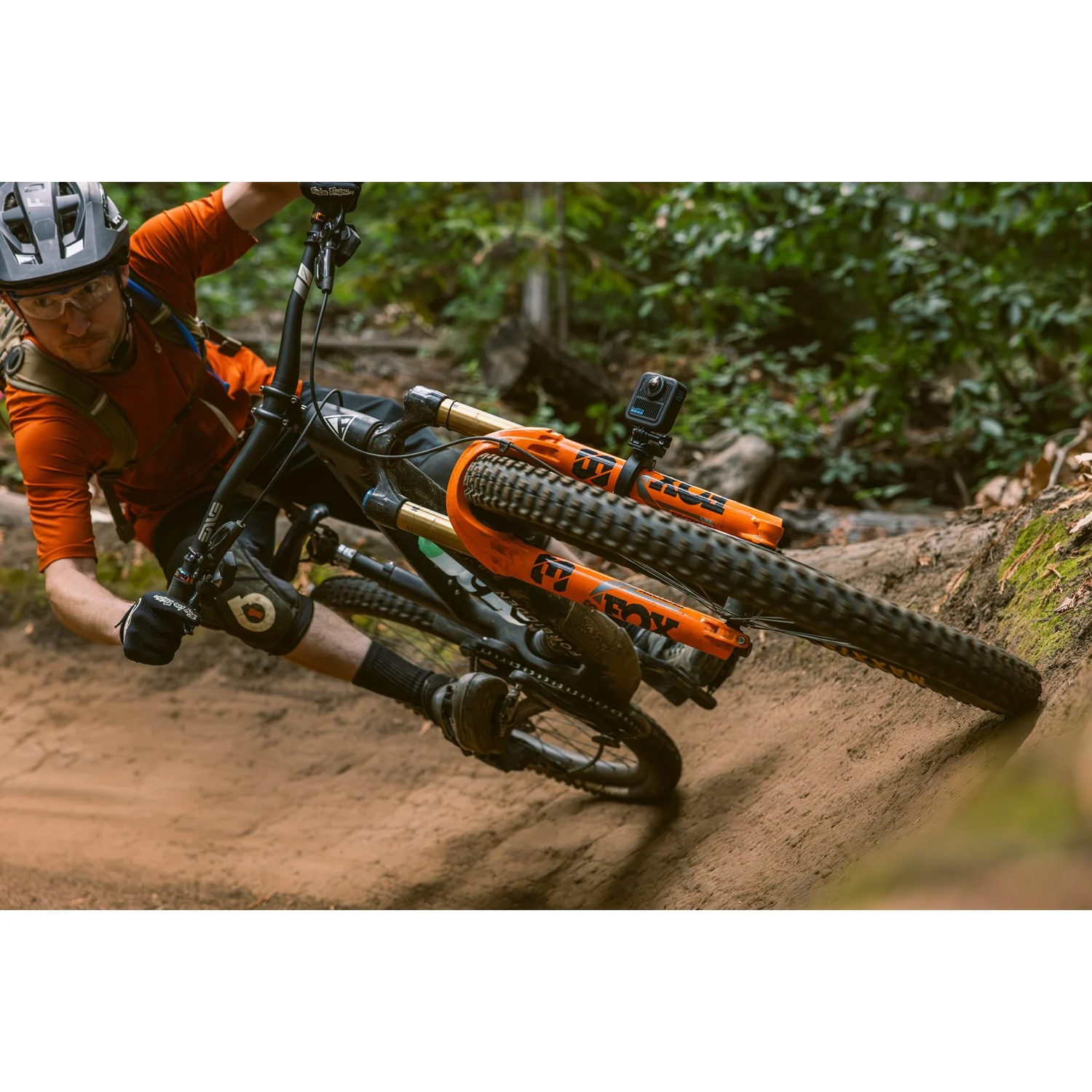Een mountainbiker rijdt over een onverharde weg. De fiets is oranje en zwart. De rijder draagt een helm, bril en een oranje shirt.
