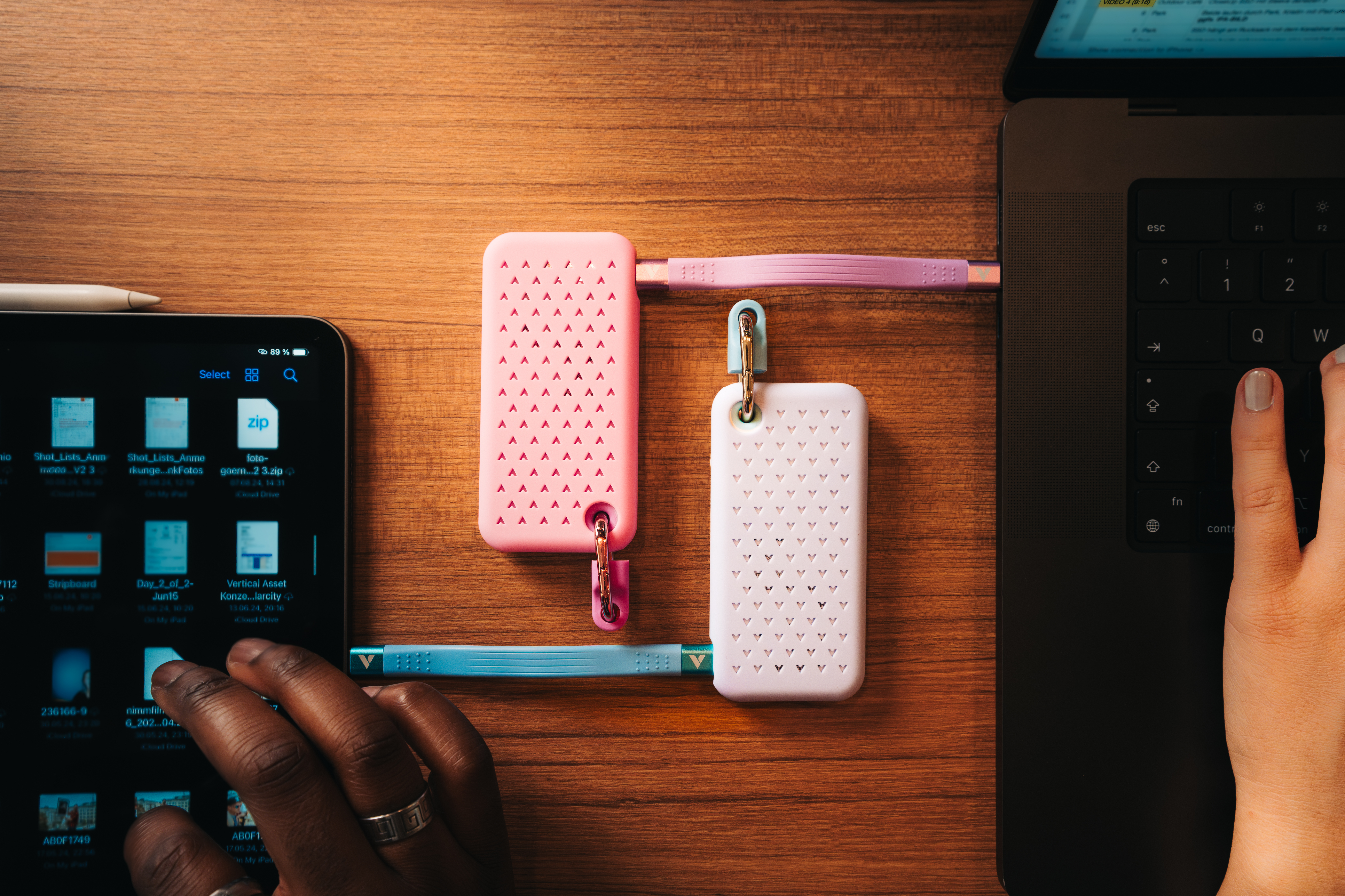 Eine Person benutzt einen Laptop und ein Tablet. Rosa und weiße technische Accessoires sind verbunden. Holz Hintergrund.