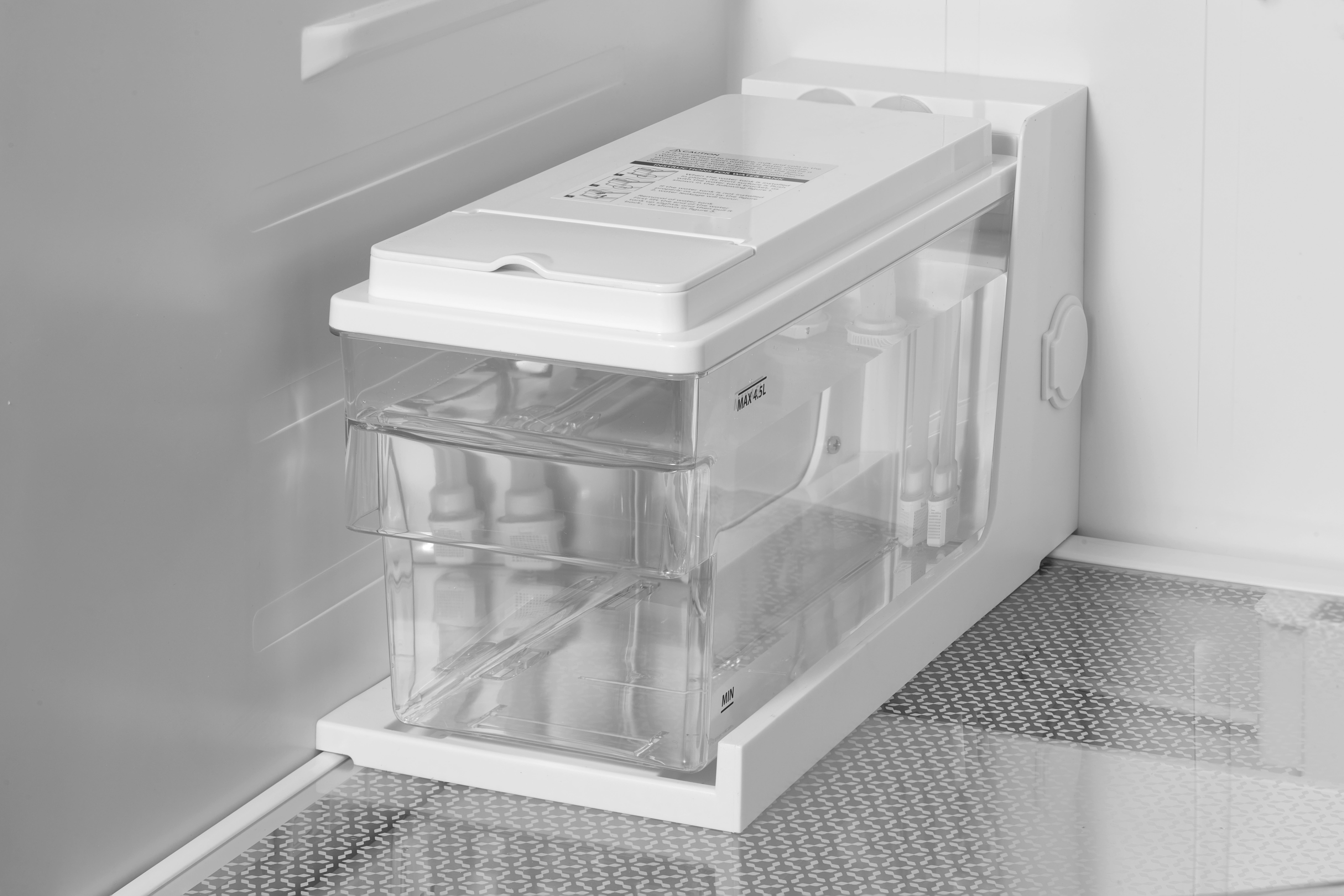 Ein weißer Wasserspender im Kühlschrank. Es hat einen transparenten Kunststoff-Wassertank mit Deckel und weißer Basis.