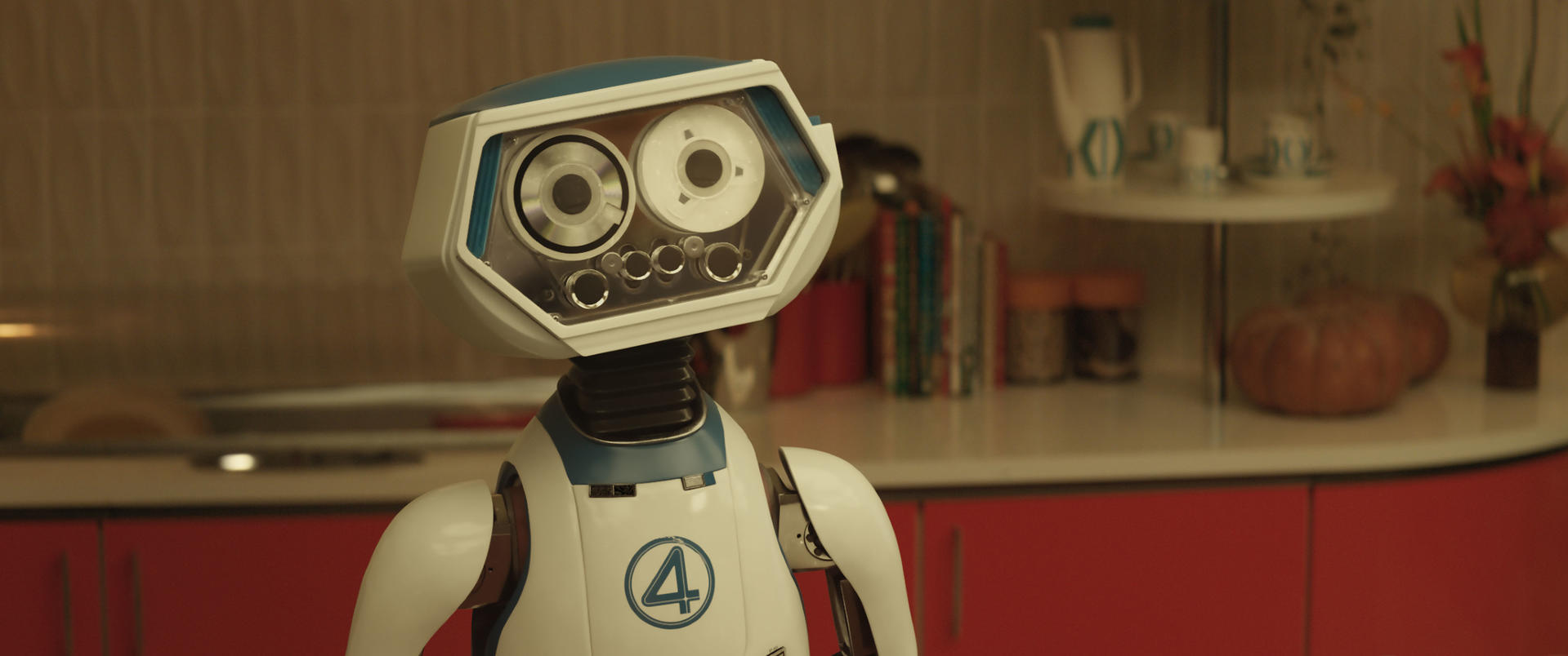 Ein Roboter mit weiß-blauem Kopf und Brust steht in einer Küche. Der Roboter hat große augenähnliche Sensoren. Ein "4"-Logo befindet sich auf seiner Brust.