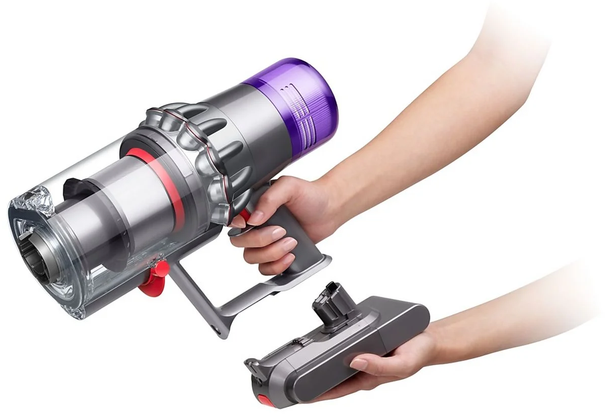 Eine Person hält einen Dyson-Staubsauger mit einem zusätzlichen Kopf. Der Staubsauger ist silber, lila und rot.