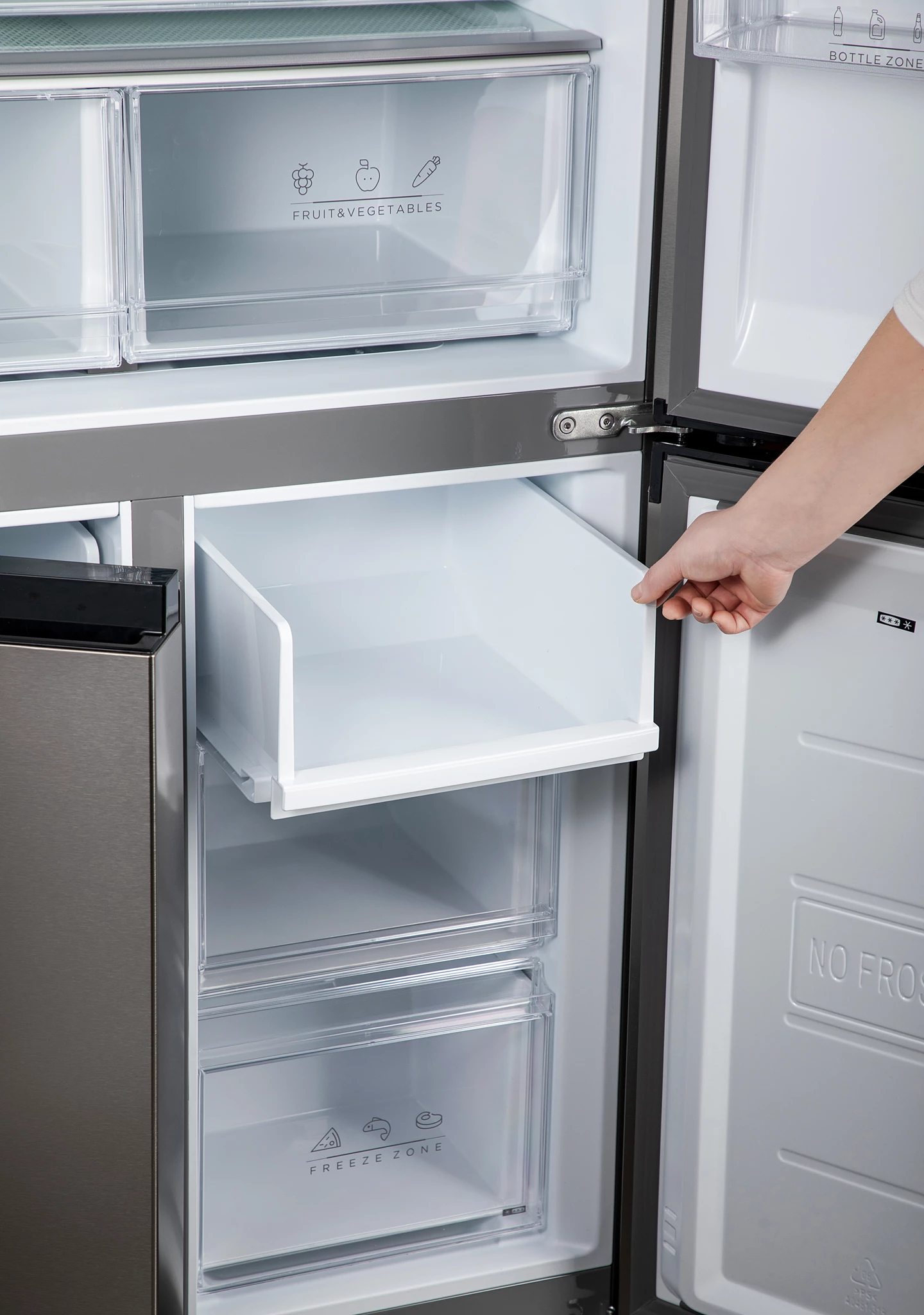 Die Hand einer Person öffnet eine Kühlschublade. Im Inneren des Kühlschranks befinden sich Regale und Schubladen für Obst, Gemüse und einen Gefrierbereich.