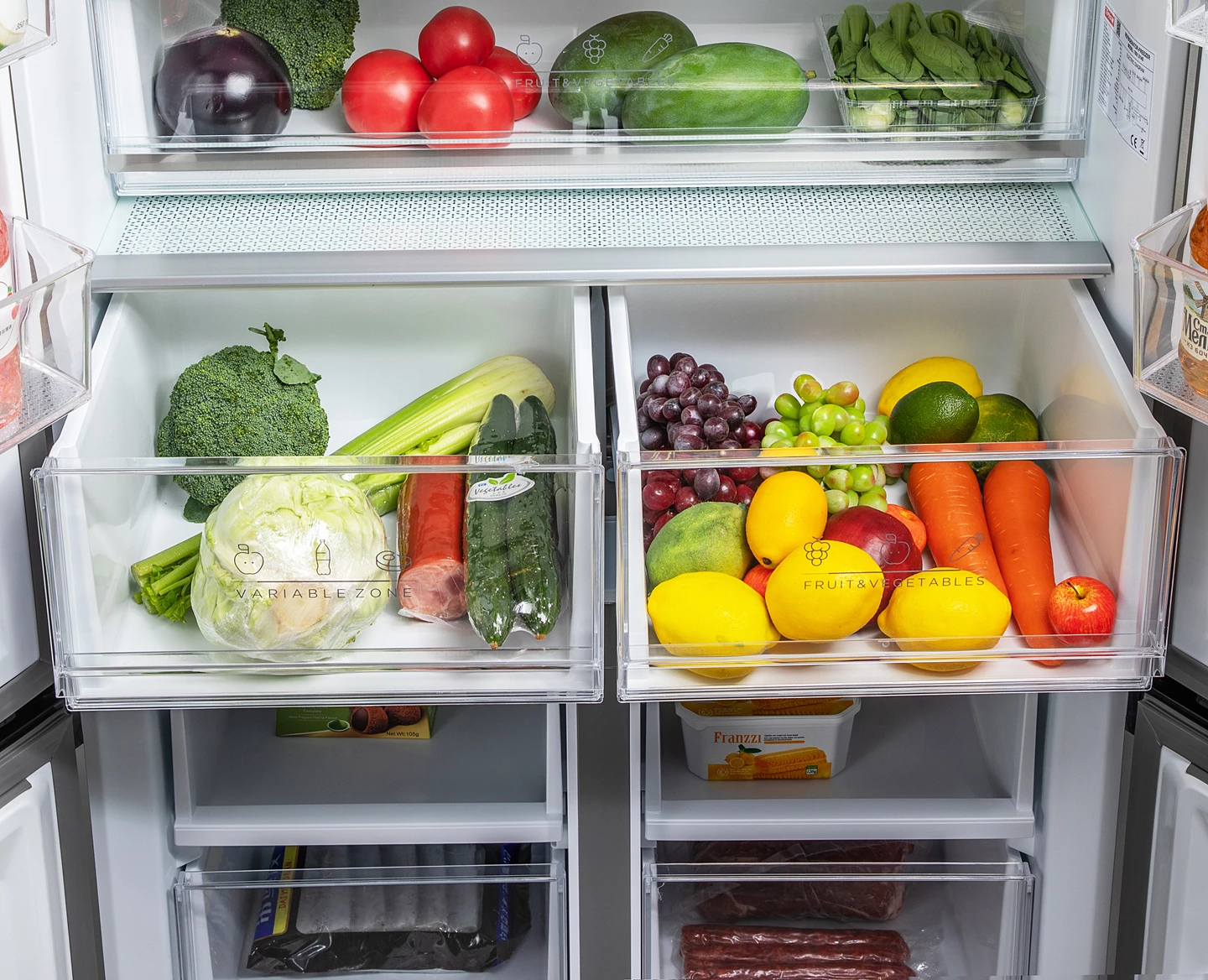Kühlschrankinnenraum gefüllt mit frischen Produkten: Tomaten, Aubergine, Brokkoli, Zitronen, Trauben, Karotten und Spinat.