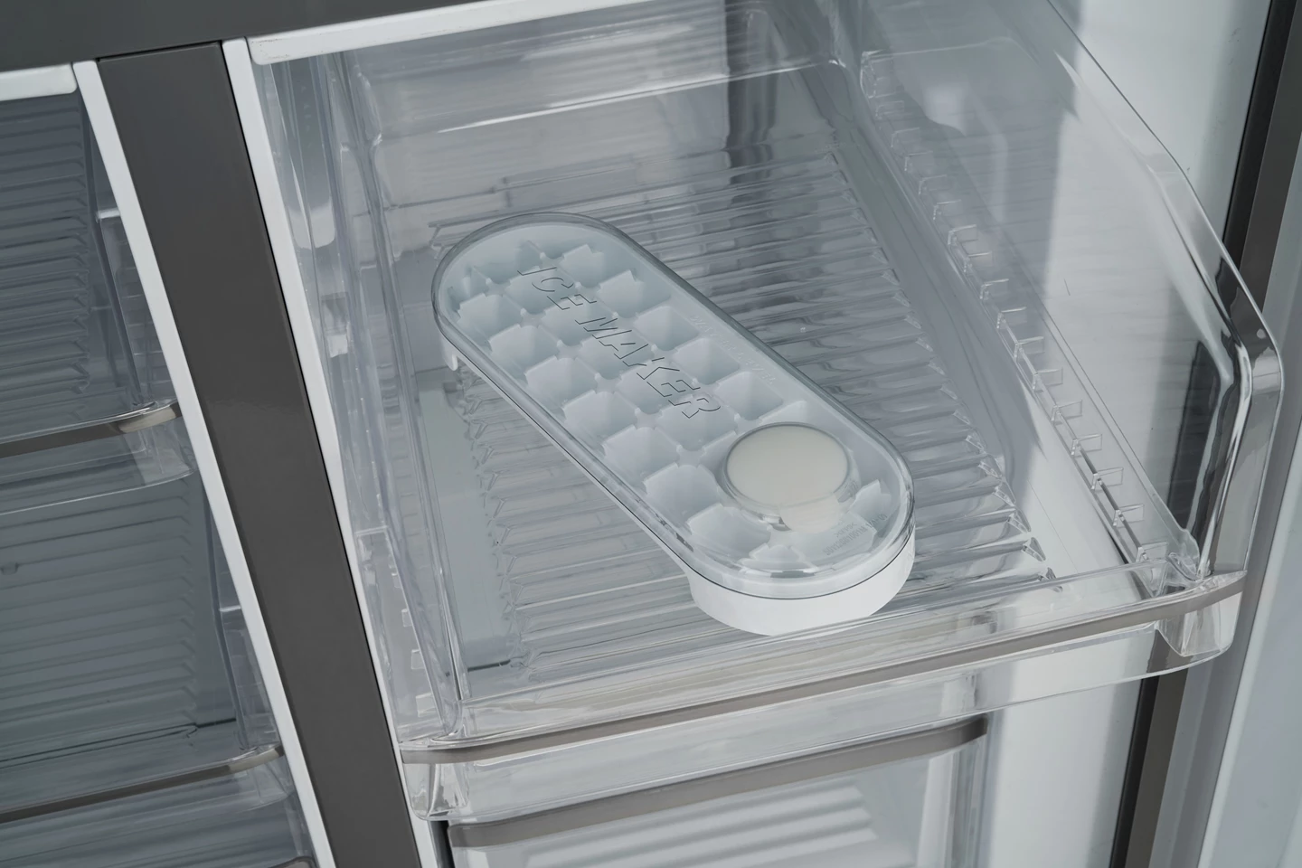 In einem Kühlschrank ist ein klarer Eisbereiter aus Kunststoff zu sehen. Der Eisbereiter liegt in einer transparenten Schublade. Die Schublade ist offen.