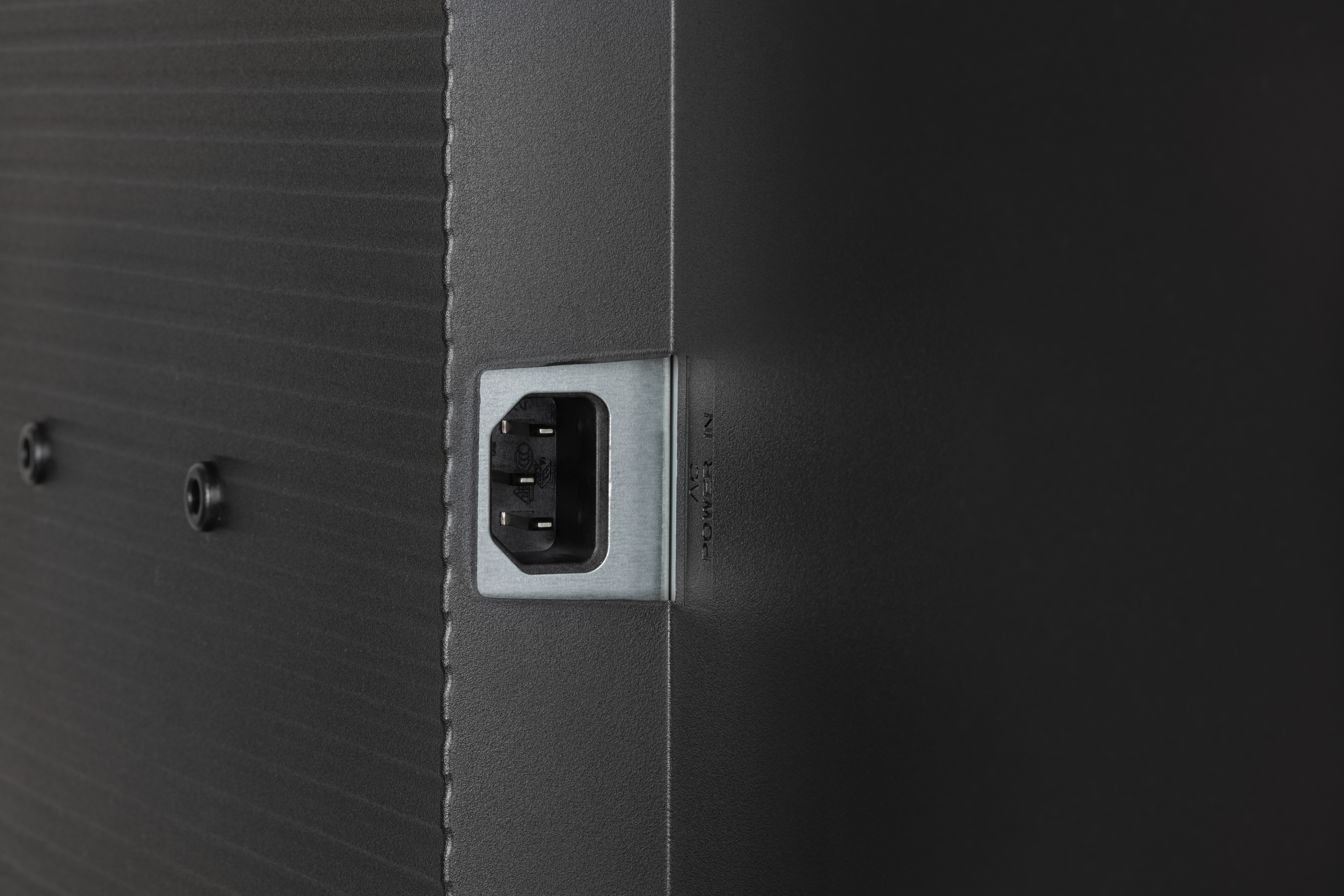 Zbliżenie czarnego wejścia zasilania na ciemnej powierzchni. Wejście zasilania AC w metalowej ramie.