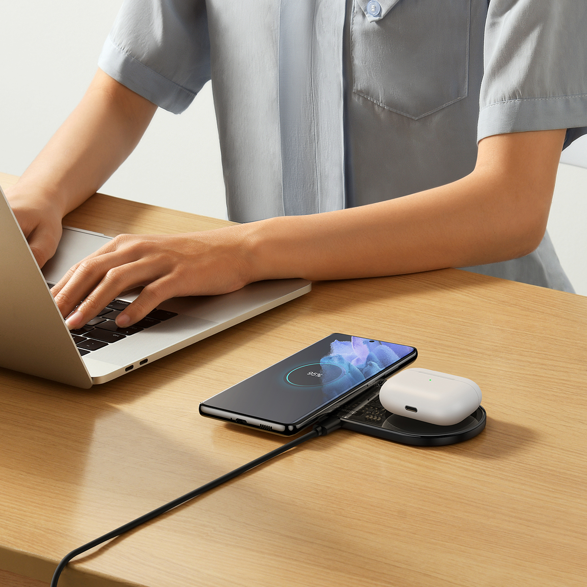 Egy személy laptopon gépel. Egy telefon, vezeték nélküli fülhallgató és egy töltőpad van az asztalon. A telefon 95%-os töltöttséget mutat.