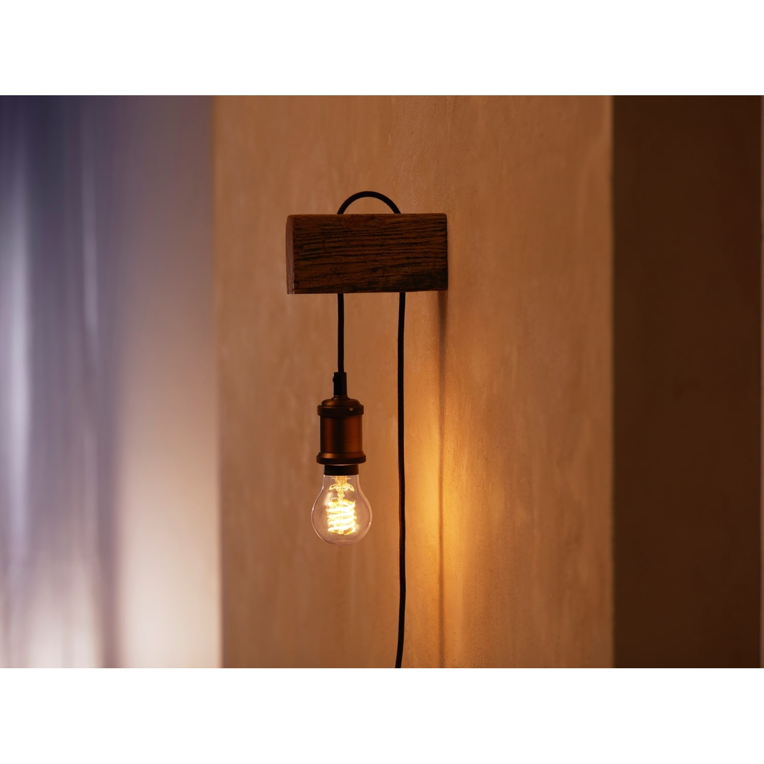 Un'applique. Un blocco di legno sostiene una lampadina con filamento visibile. Un filo nero si collega al muro.