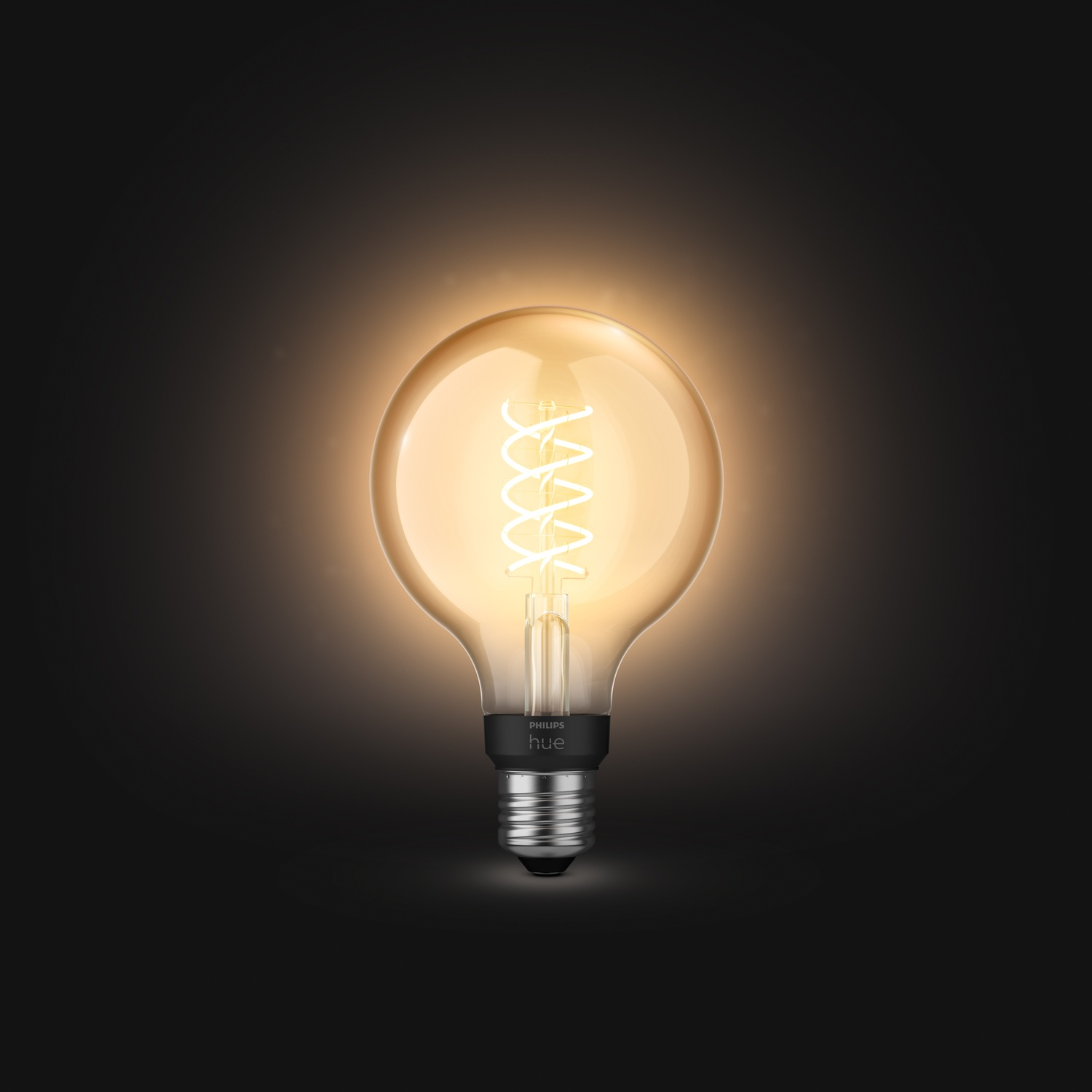 Una lampadina rotonda e luminosa con filamento a spirale, su sfondo scuro. La base riporta 'Philips hue'.