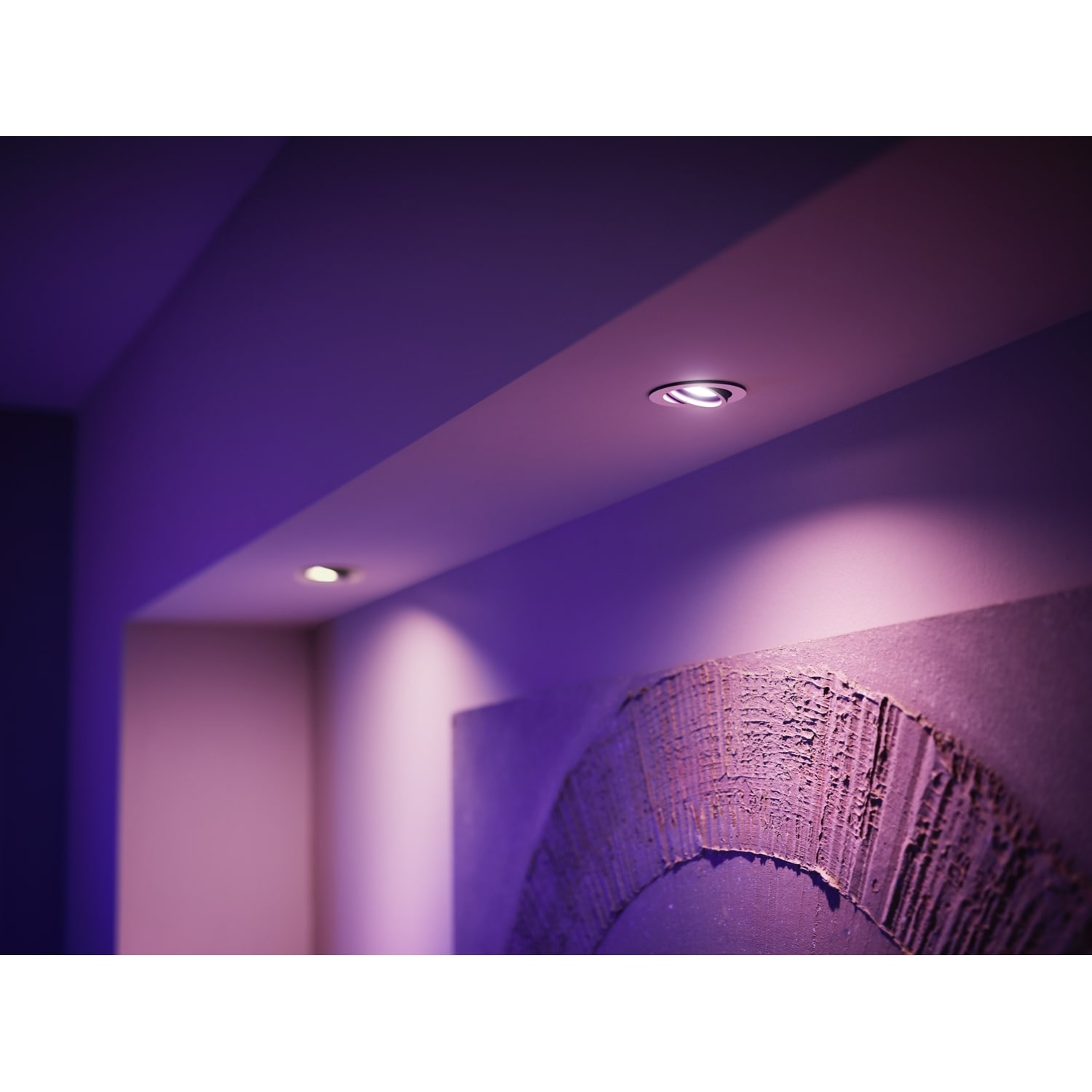 Stanza illuminata di viola con faretti a incasso sul soffitto. Un'opera d'arte strutturata è sulla parete. La scena è moderna e minimalista.