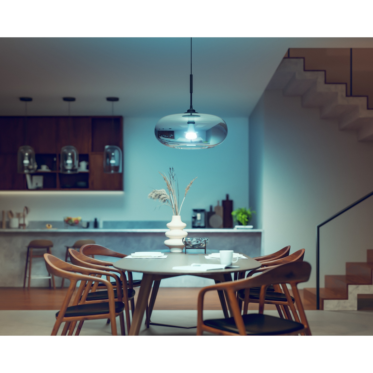 Una sala da pranzo moderna con tavolo rotondo, sedie e una lampada a sospensione. Sullo sfondo, una cucina e una scala sono visibili.