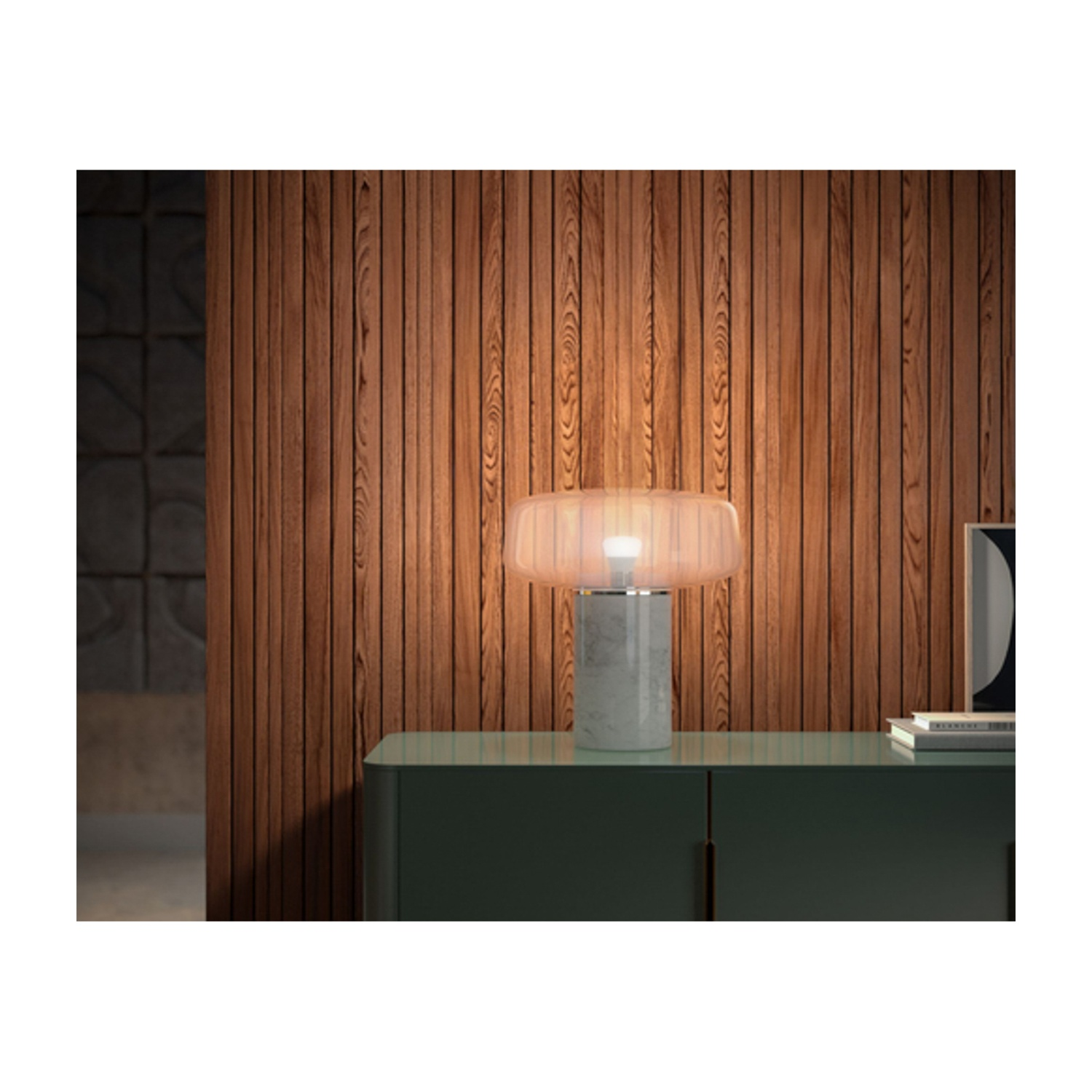 Una lampada da tavolo con base in marmo e paralume in vetro smerigliato su un mobile verde. Sfondo parete in legno.