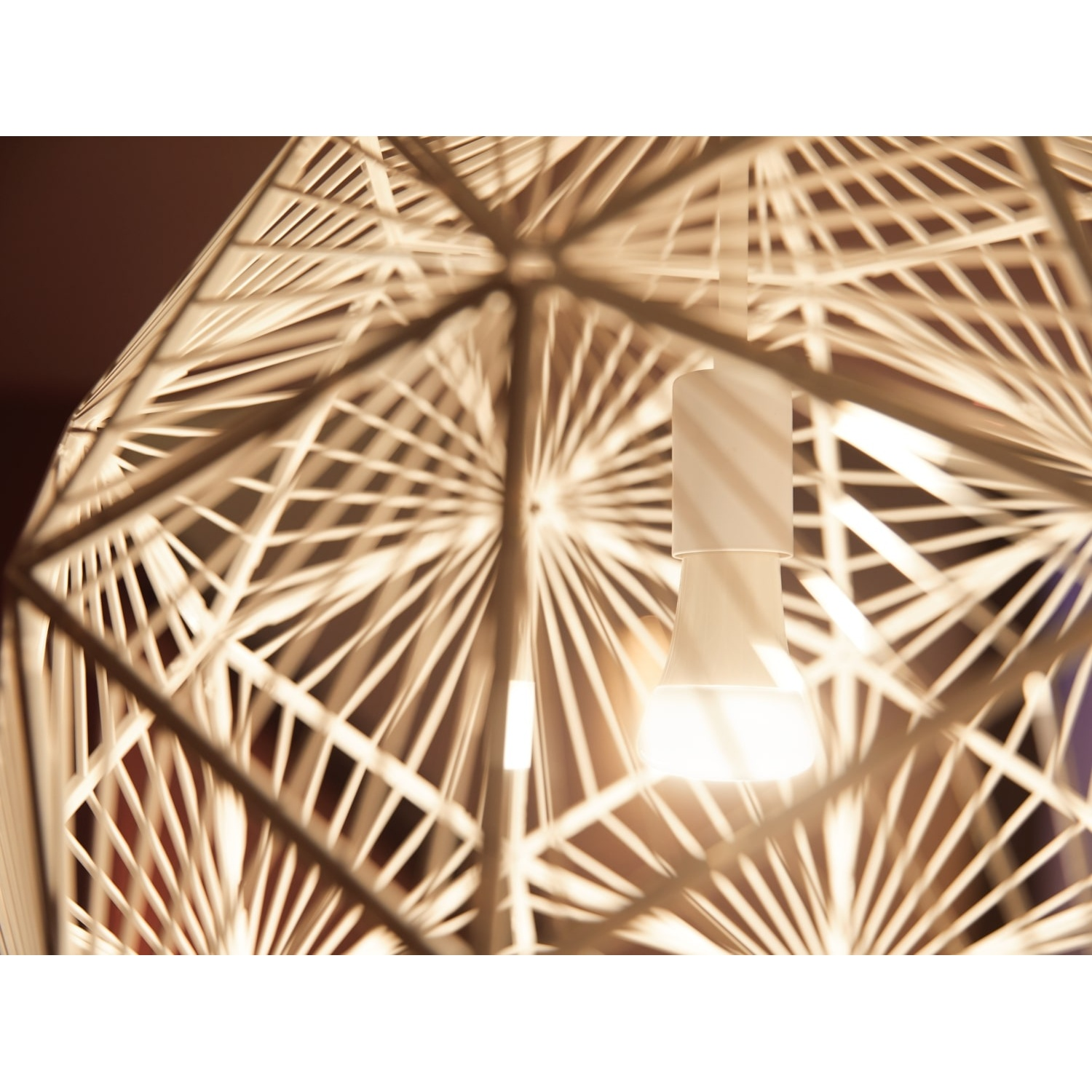 Primo piano di una lampada a sospensione moderna e geometrica con una lampadina accesa. Il telaio ha un design bianco a forma di ragnatela.