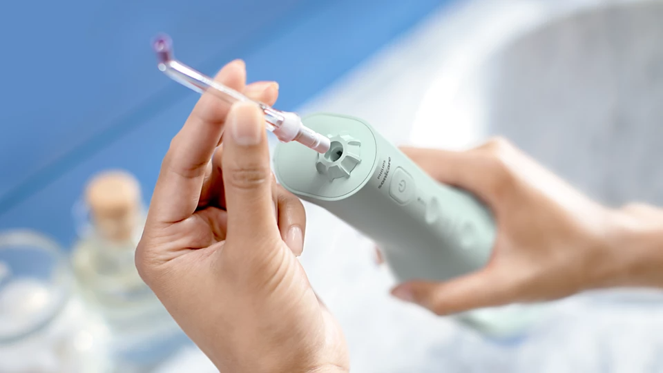 Személy egy átlátszó hegyet helyez be egy világoszöld Philips Sonicare készülékbe. A háttér elmosódott, kék árnyalattal.