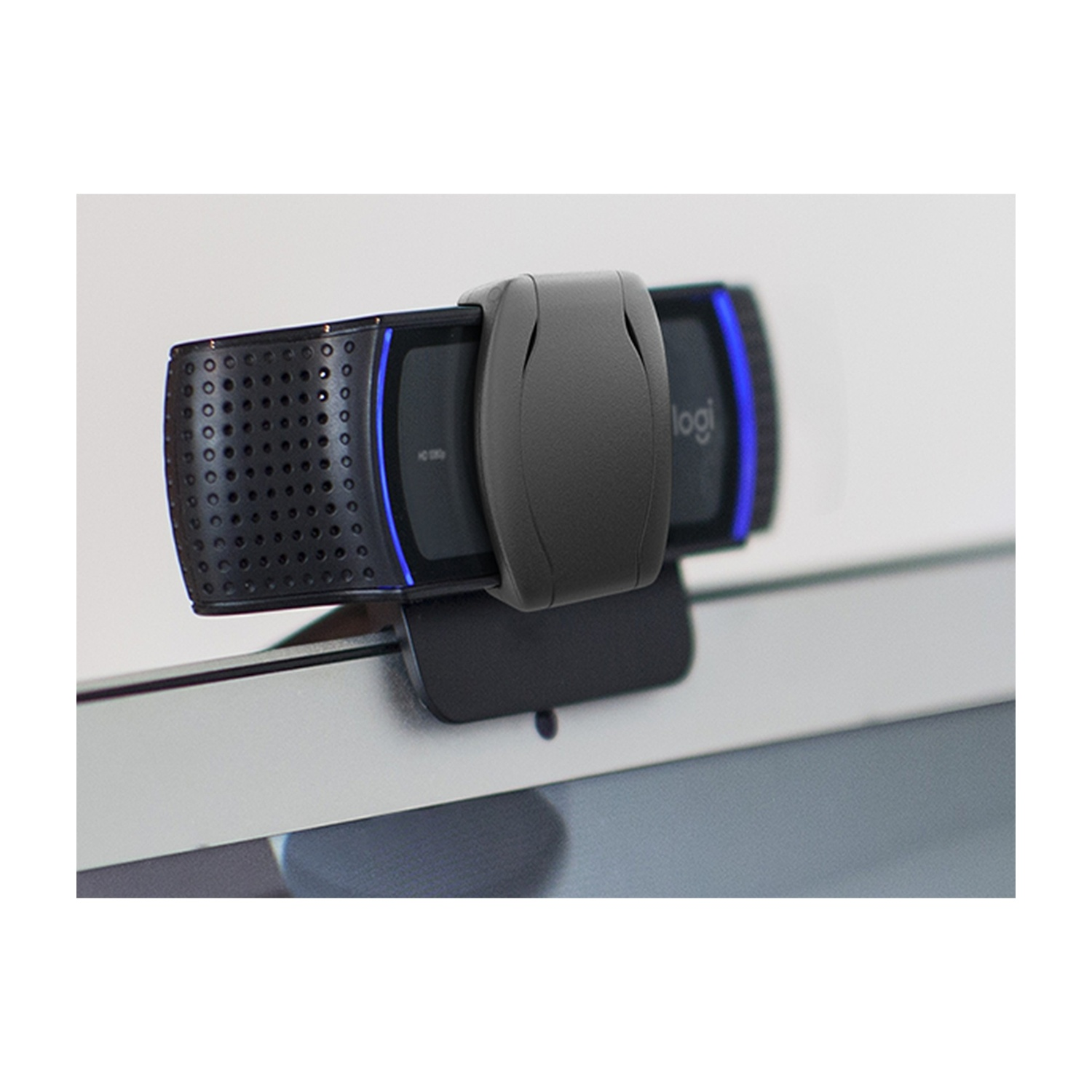 Una webcam nera collegata allo schermo di un laptop. La webcam ha un corpo grigio scuro e il logo del marchio. Lo sfondo è bianco.