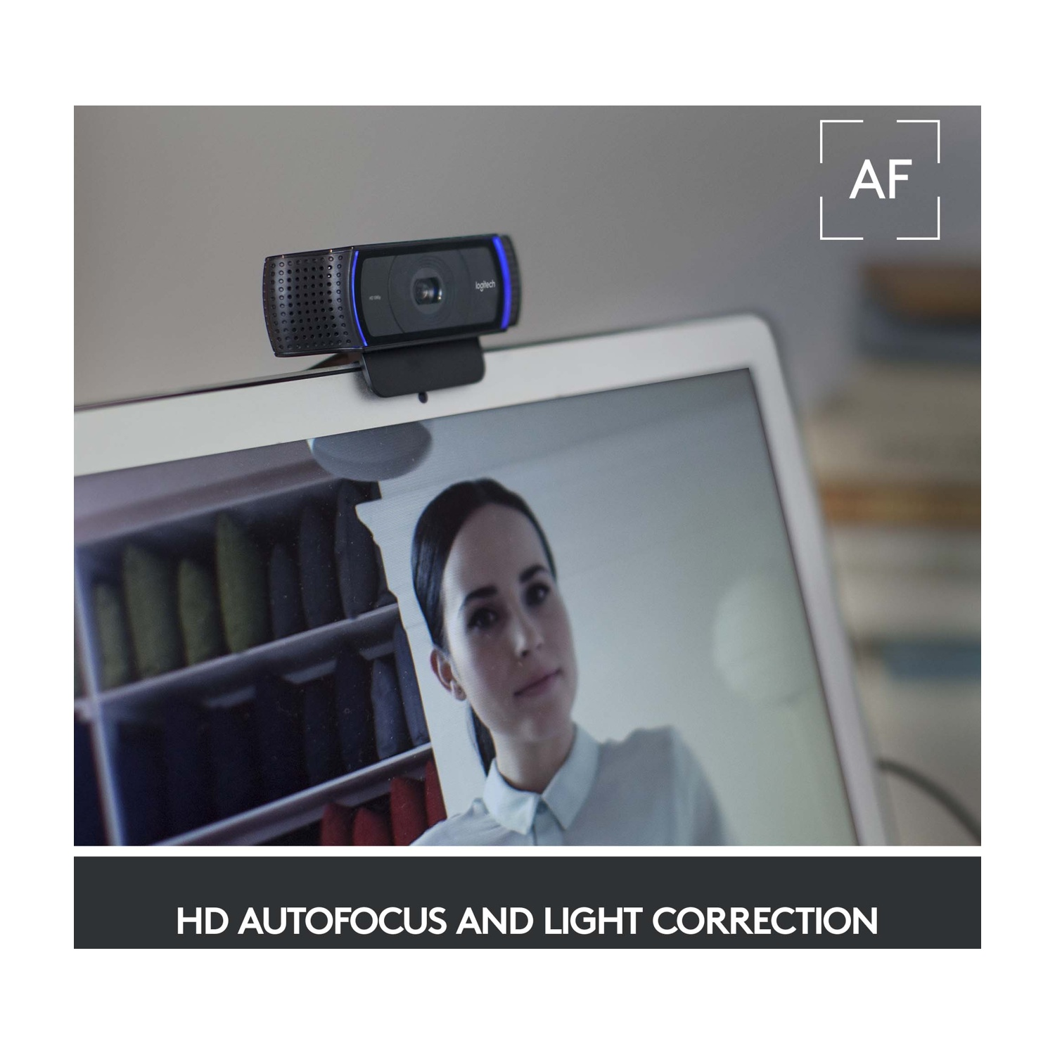 Una webcam Logitech è sopra un laptop, che mostra una donna. Lo schermo mostra il riflesso di un armadio. Testo: 'HD AUTOFOCUS AND LIGHT CORRECTION'.