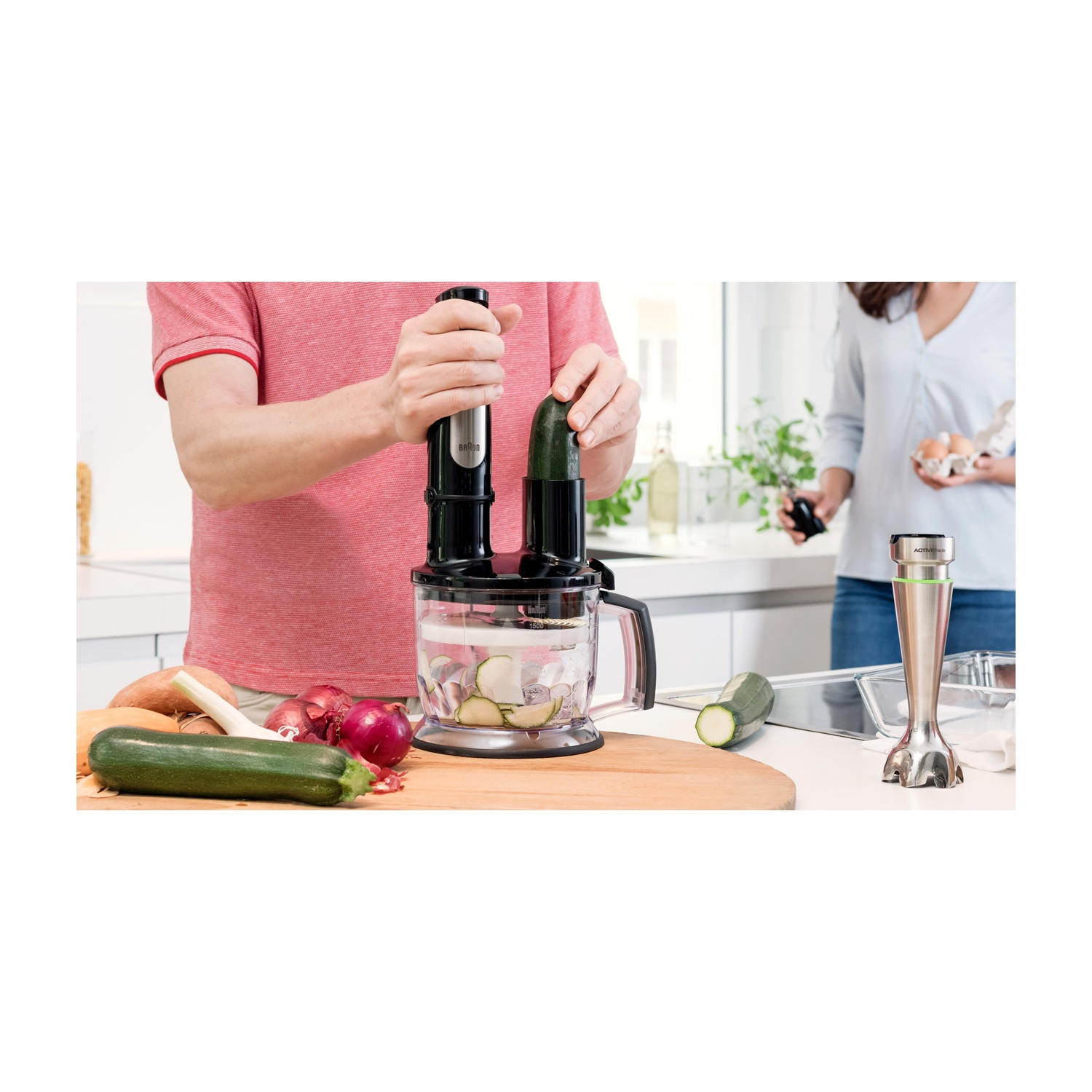 Persona che prepara verdure con un robot da cucina. Zucchine, cipolle e altri ingredienti su un tagliere di legno.