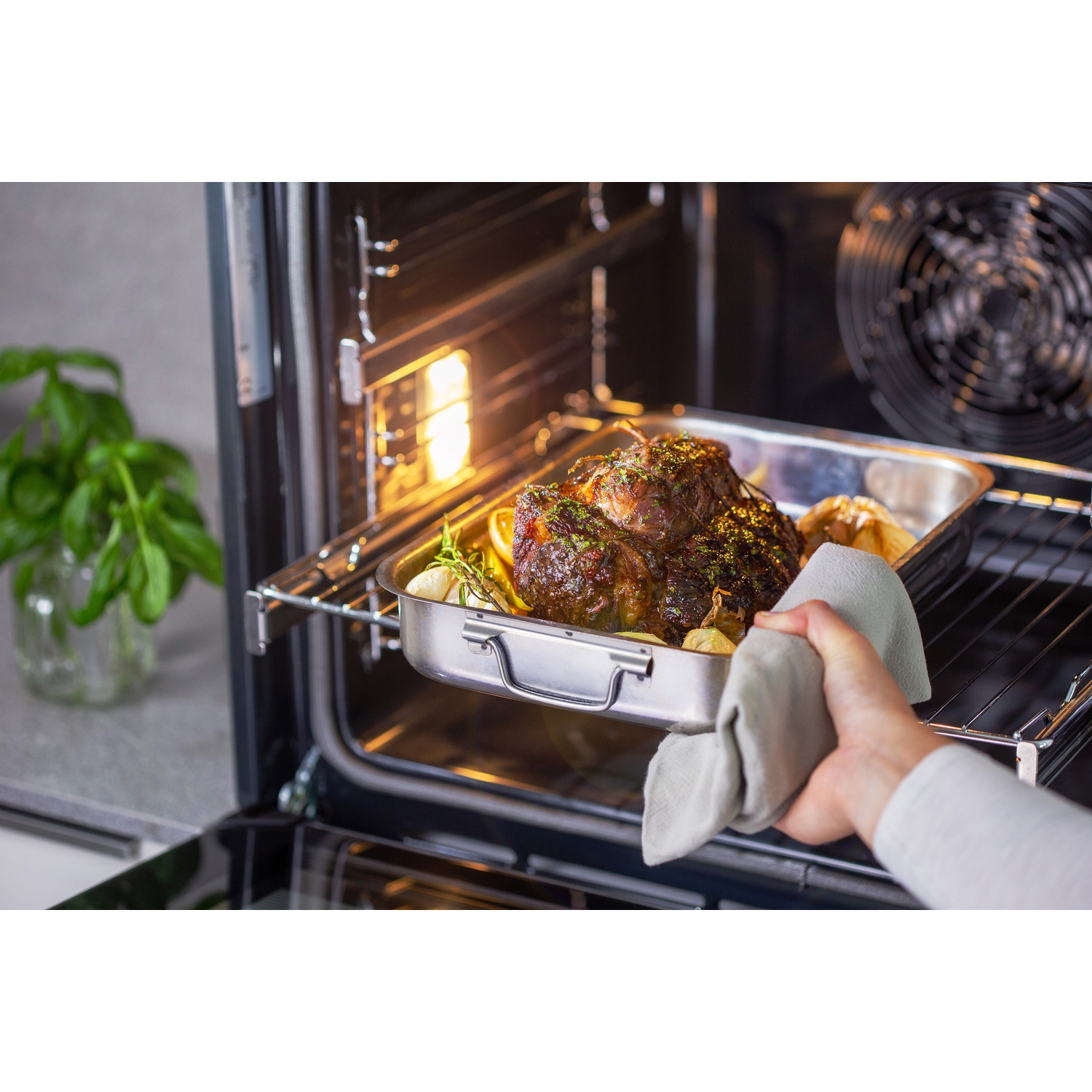 Una persona toglie carne arrosto dal forno. La carne è in una teglia di metallo con aglio ed erbe.