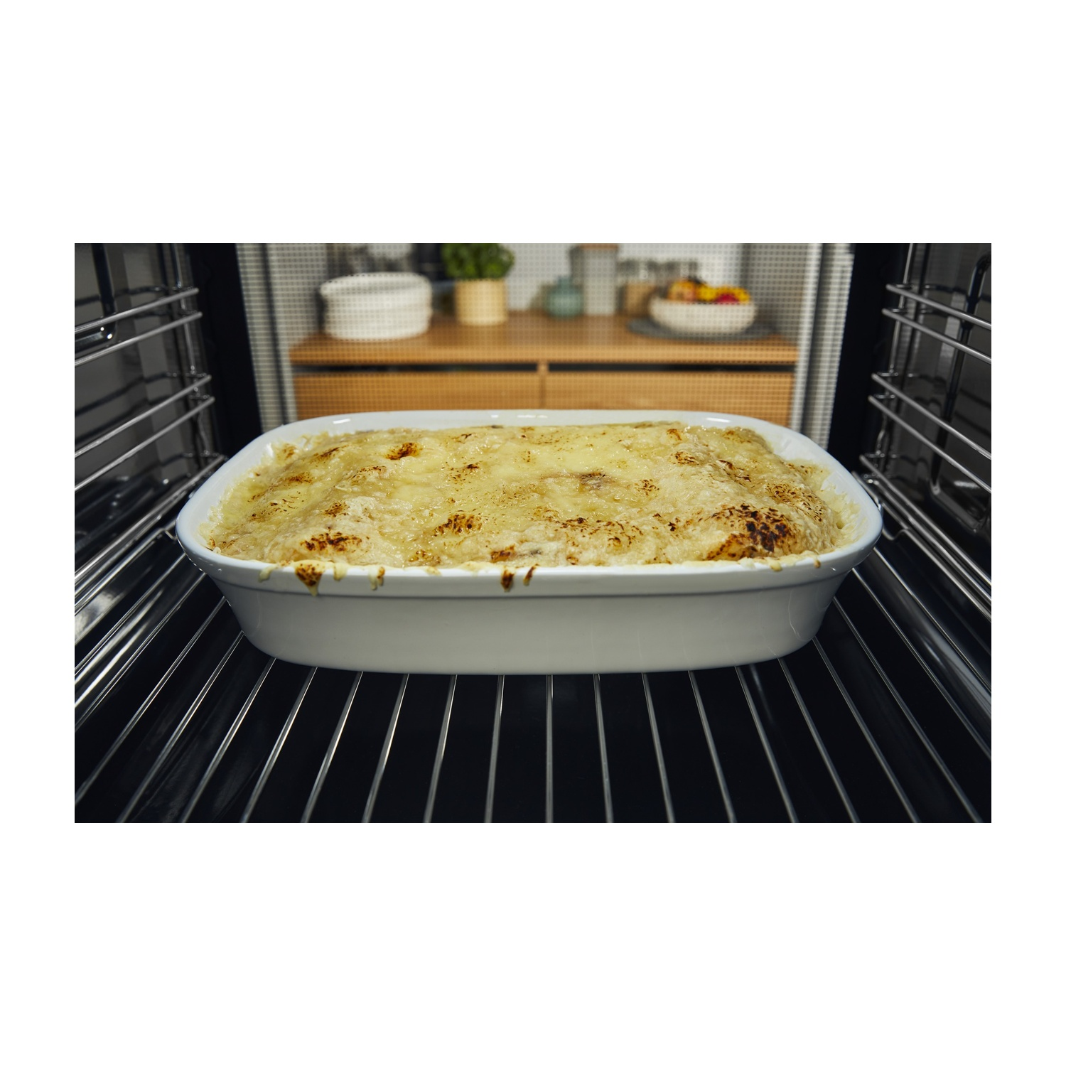 Una pirofila con cibo al forno è all'interno di un forno. Il piatto è bianco, il cibo è dorato. Il forno è nero con griglie metalliche.