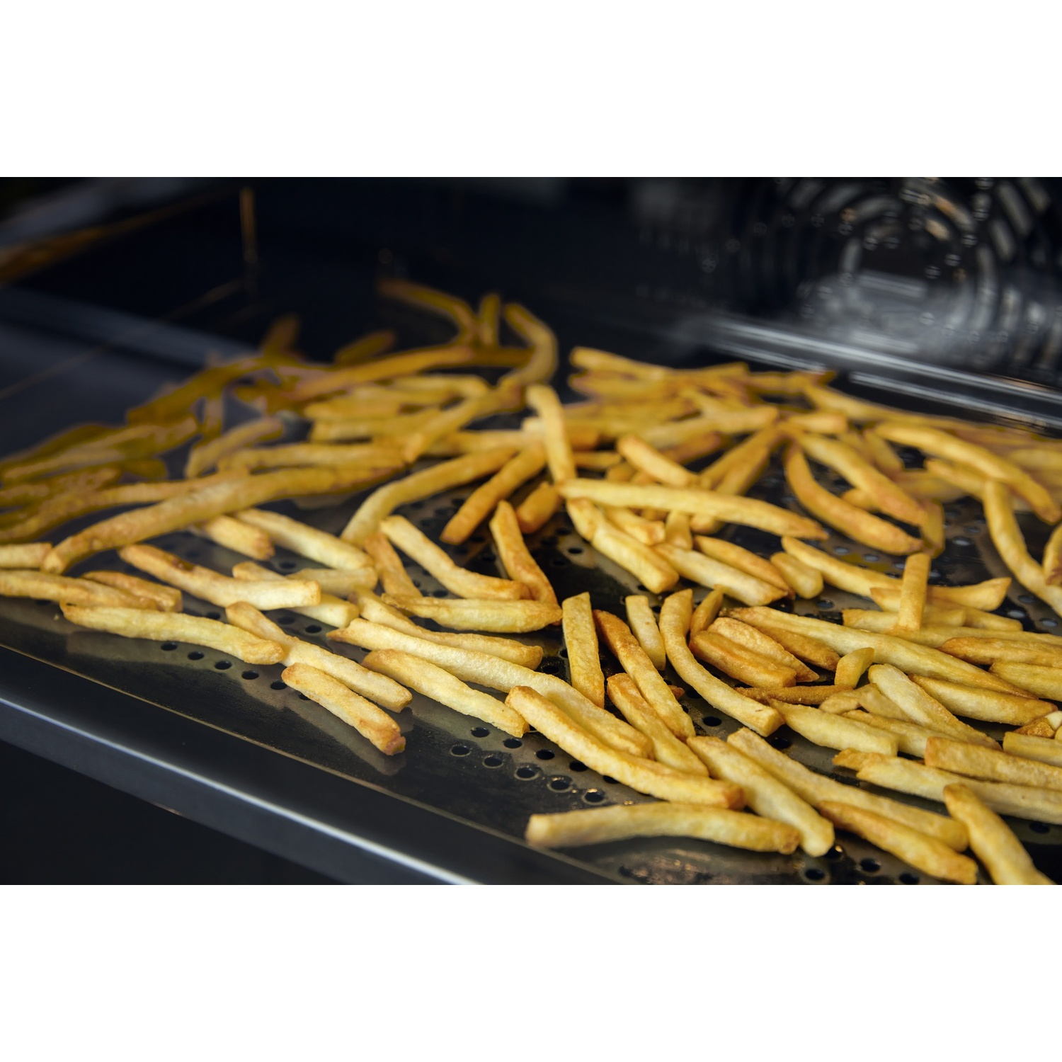 Patatine fritte dorate su un vassoio di metallo perforato all'interno di un forno. Le patatine sono sparse, riempiendo il vassoio.