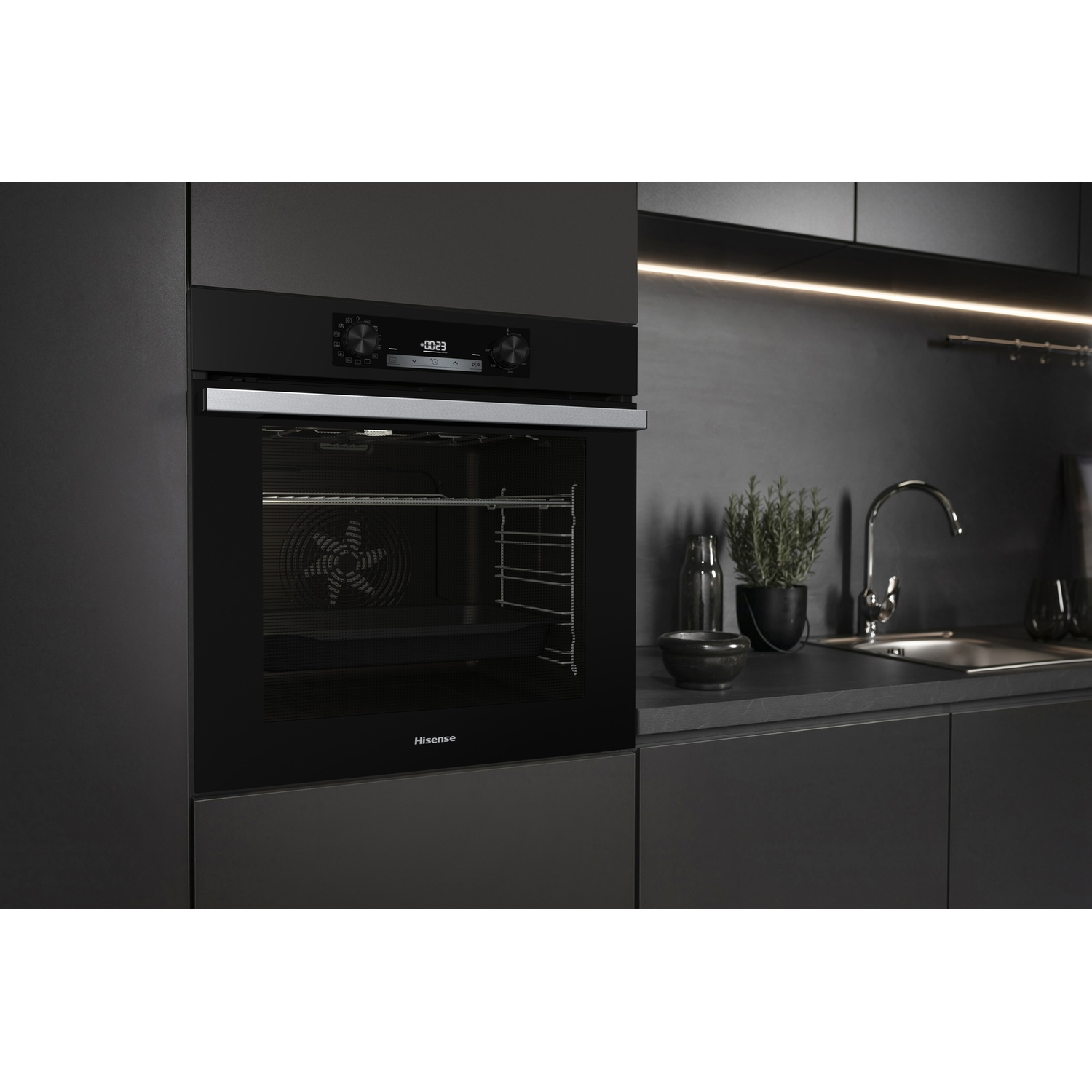 Un moderno forno nero è centrato, con un display del timer. A destra un lavandino in acciaio inossidabile, una pianta e bottiglie.