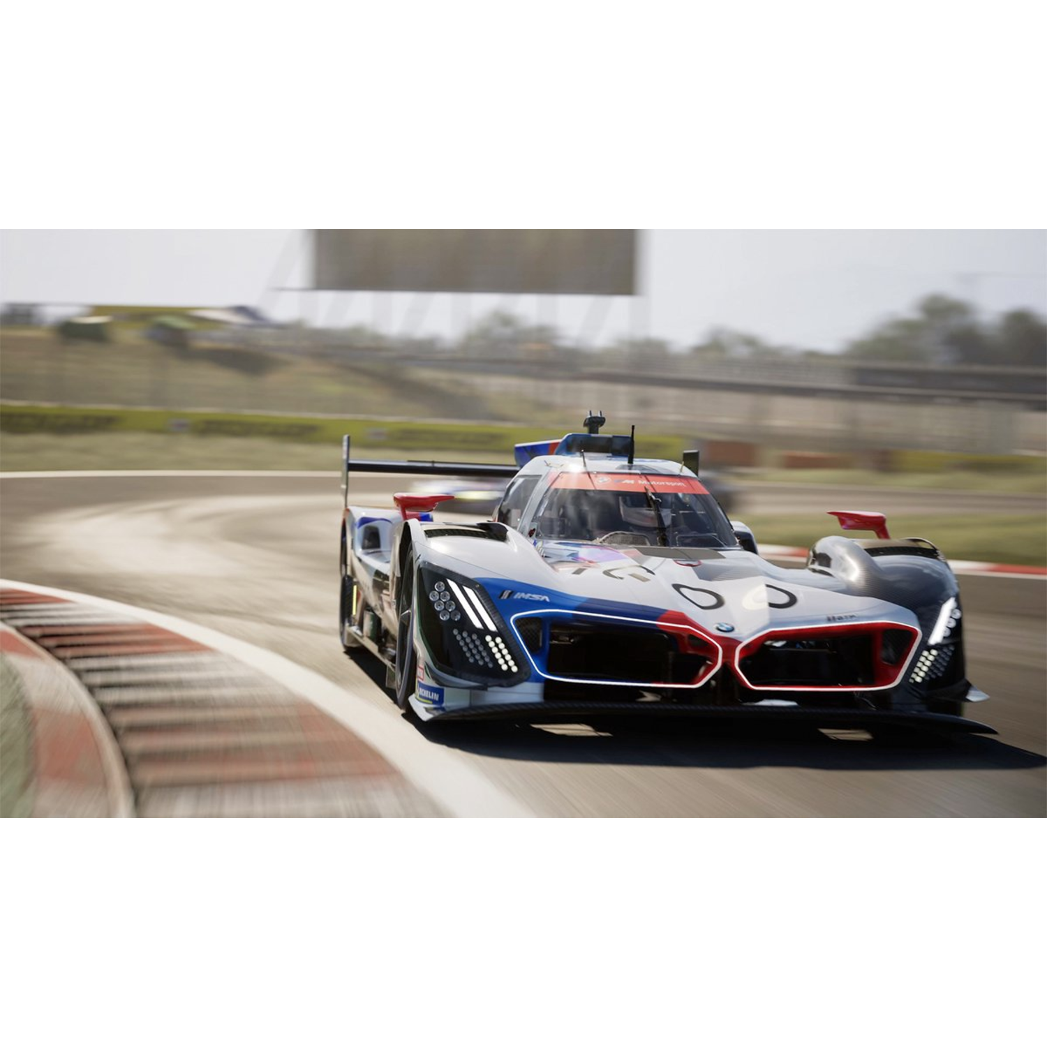 A race car speeds around a track corner. It is white, blue, and red. The background has a blurred racetrack and greenery.
