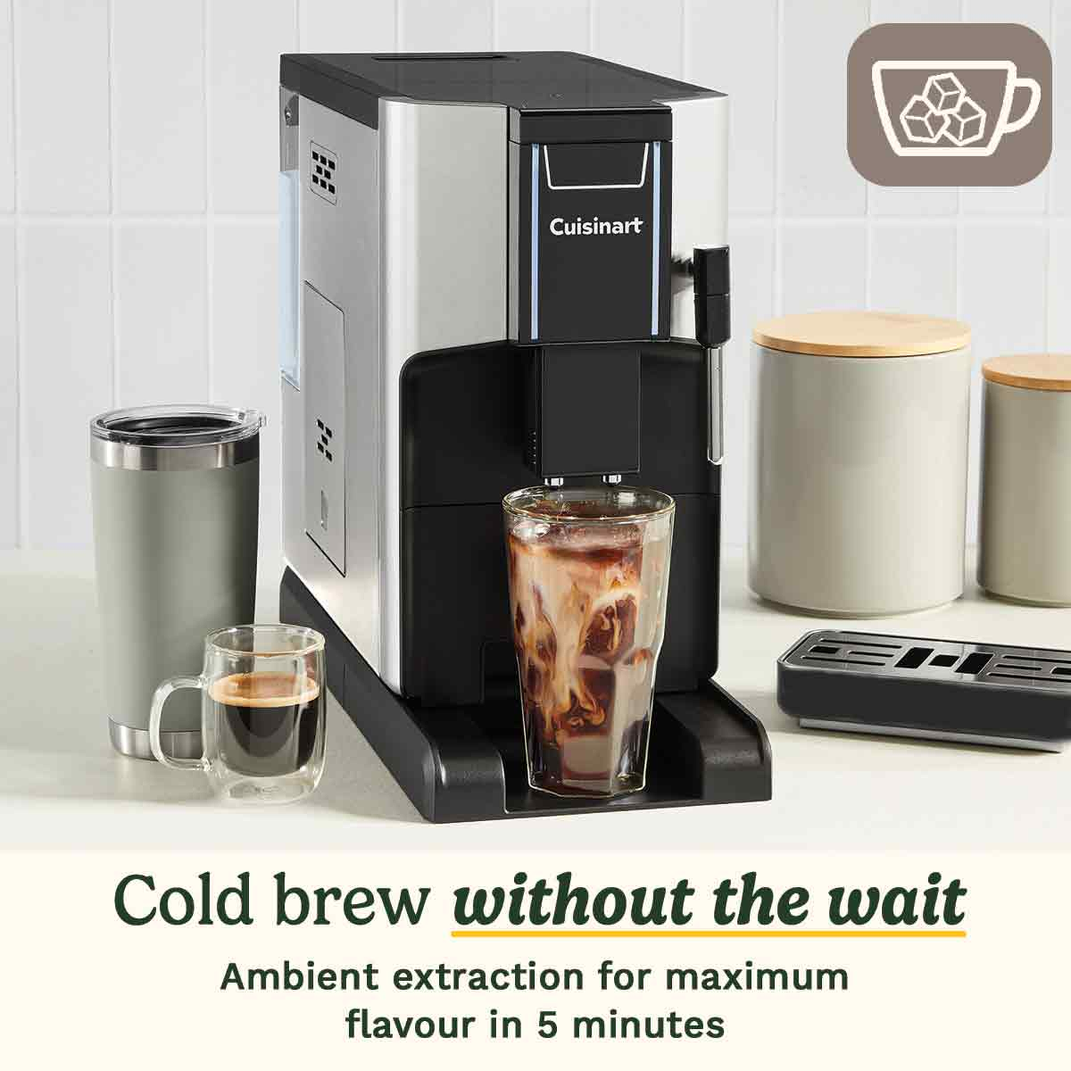 A silver and black Cuisinart cold brew machine with a glass of iced coffee. A mug with espresso and a tumbler sit nearby.