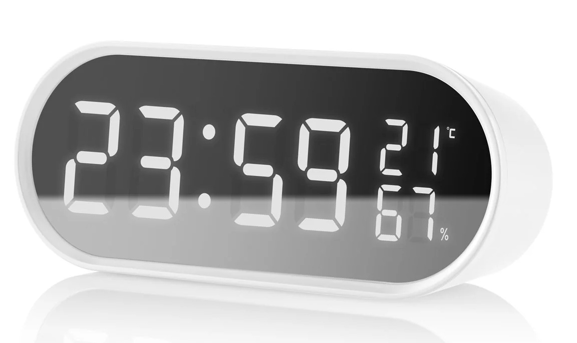 Biały zegar cyfrowy wyświetla 23:59, 21 stopni Celsjusza i 67% wilgotności. Ma zaokrąglony prostokątny kształt.