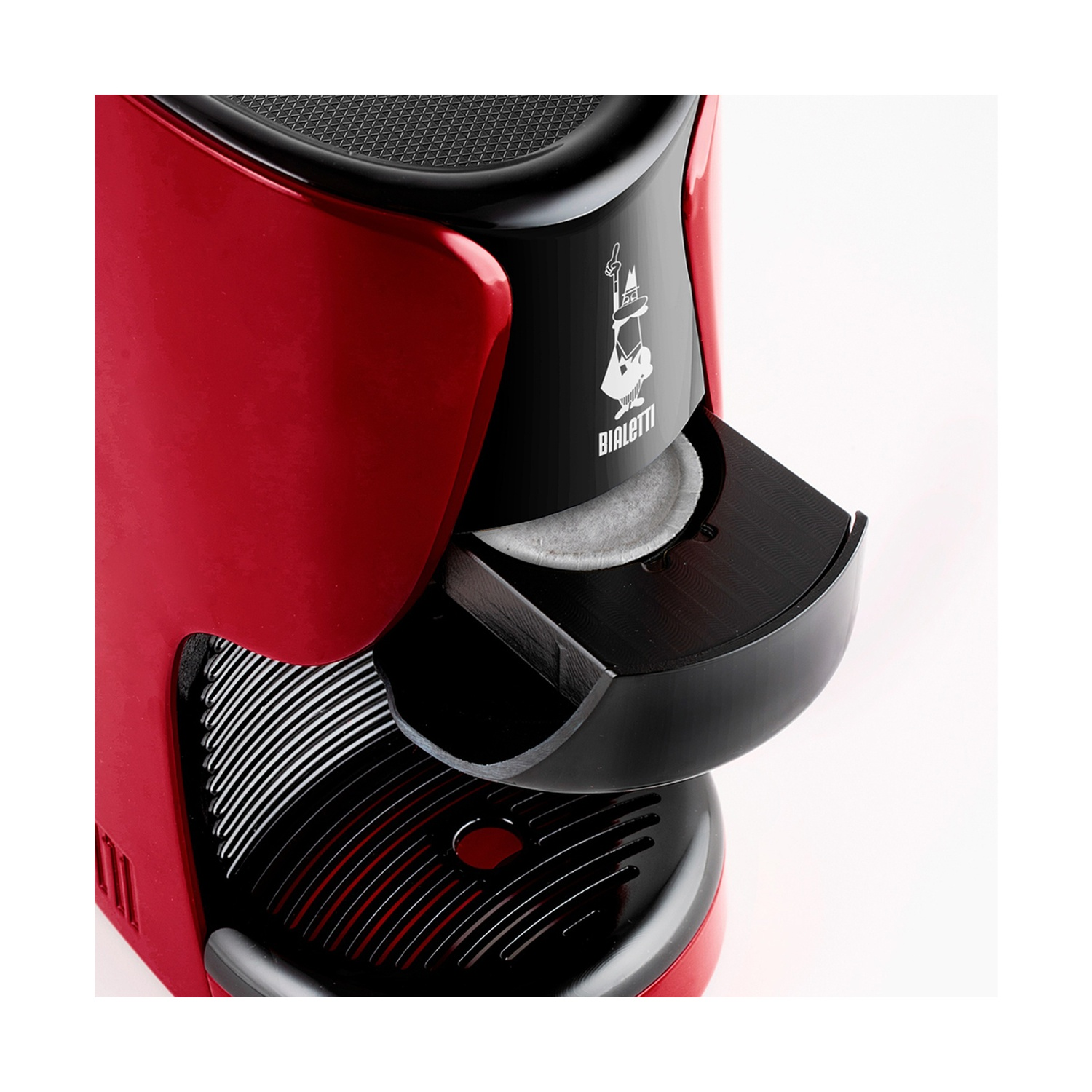 Una macchina da caffè Bialetti rossa e nera. Una cialda di caffè è nel vassoio. La macchina ha una parte superiore e un vassoio neri.