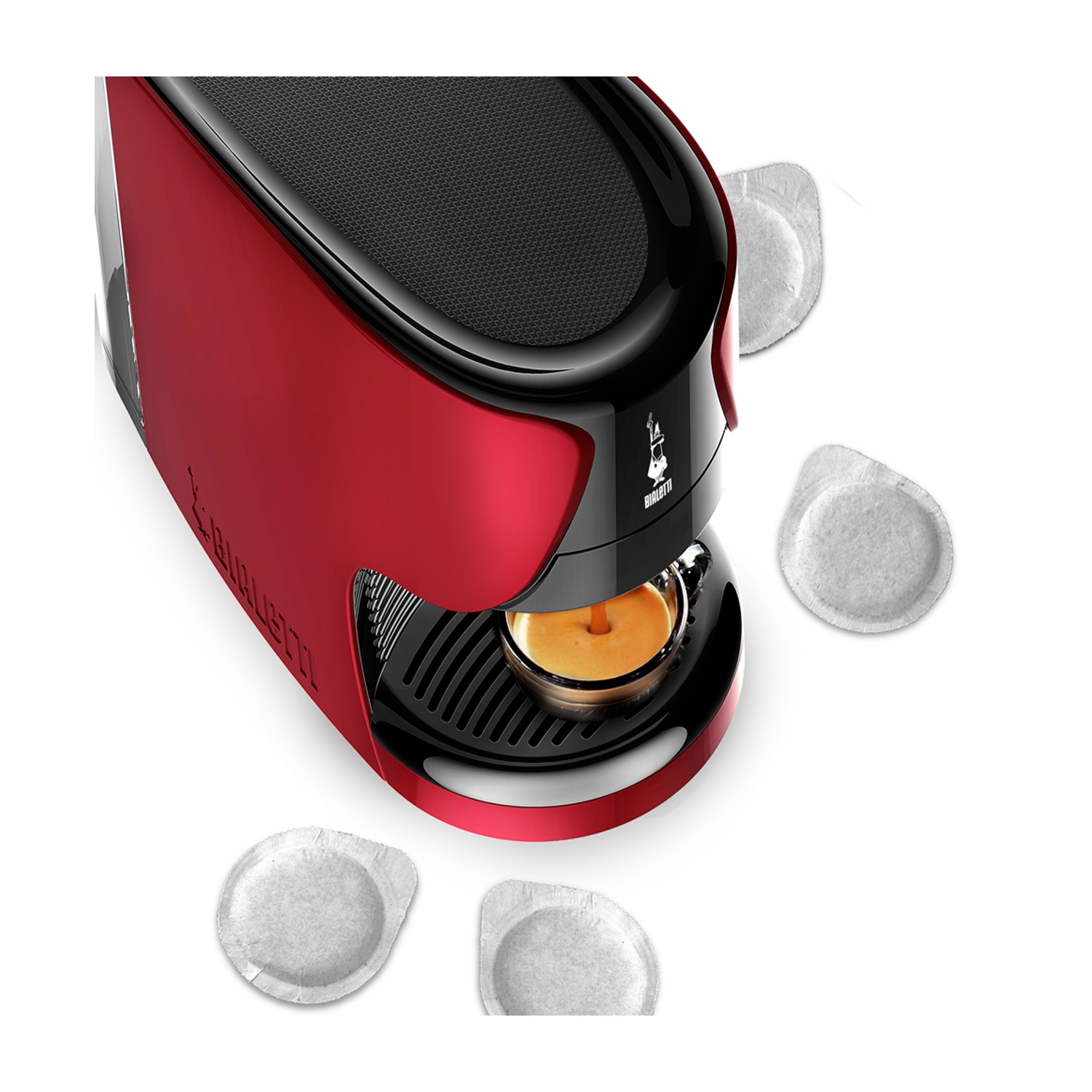 Una macchina per espresso rossa con dettagli neri sta preparando il caffè. Le cialde di caffè sono sparse intorno alla macchina. Lo sfondo è bianco.