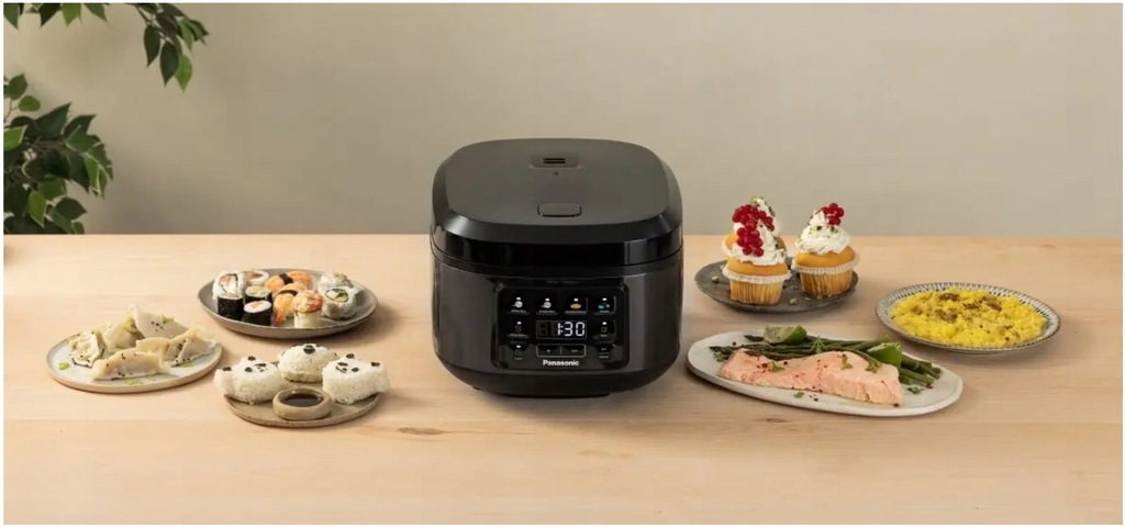 Czarny garnek do gotowania ryżu jest otoczony różnymi daniami: sushi, pierożkami, babeczkami, łososiem i ryżem. Wszystko stoi na drewnianym stole.