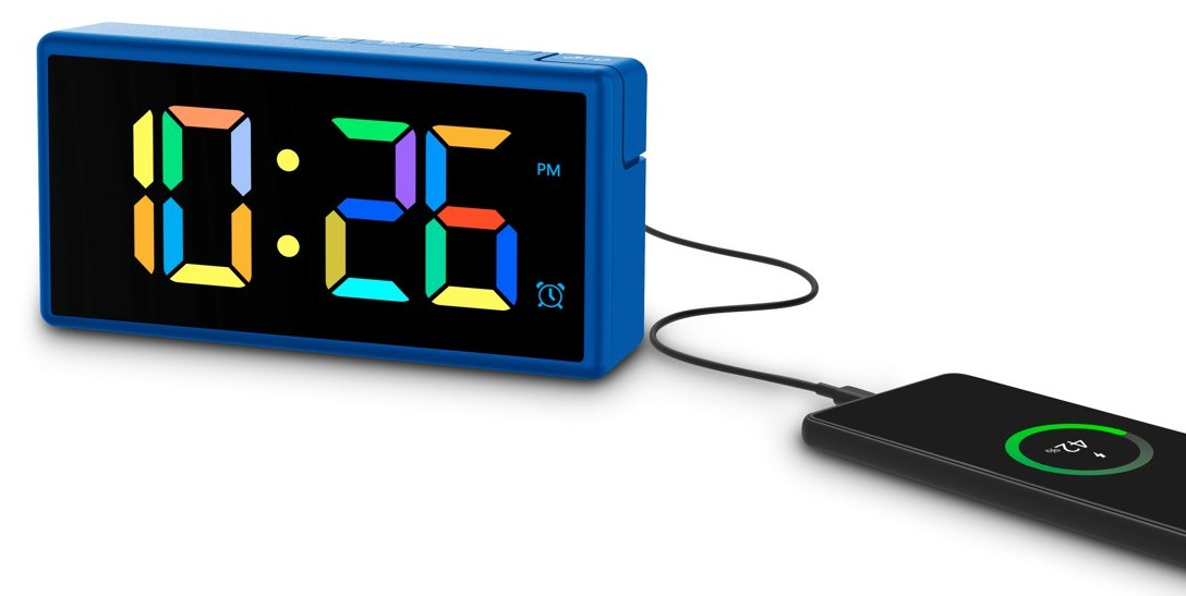Niebieski cyfrowy budzik wyświetla godzinę 22:26. Czarny telefon ładuje się za pomocą kabla. Telefon pokazuje zieloną baterię.