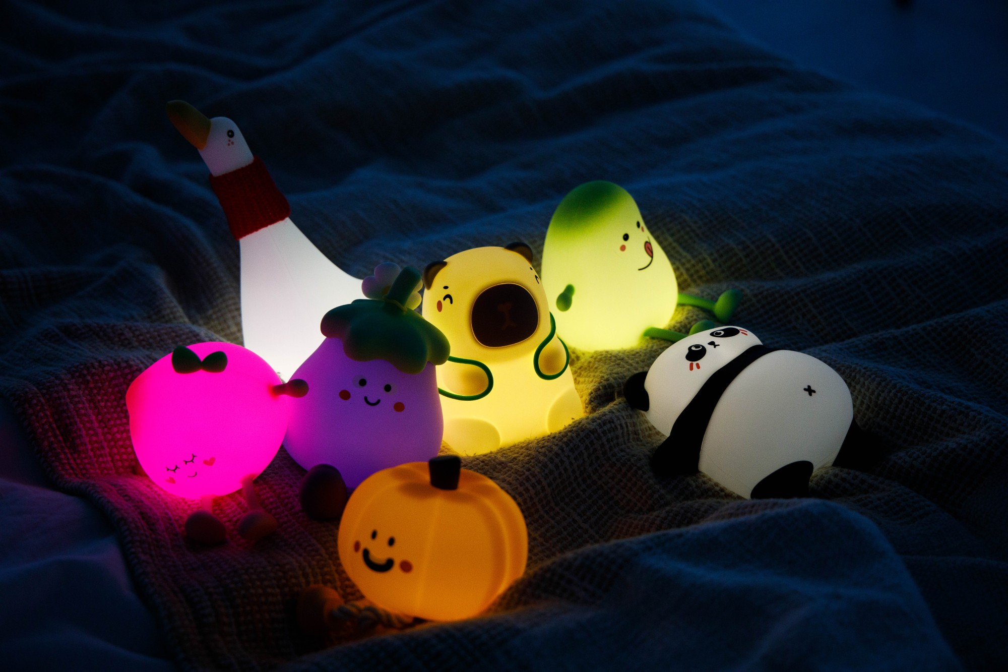 Świecące lampy z kreskówek przedstawiające gęś, niedźwiedzia, gruszkę, bakłażana, dynię i pandę na kocu. Kolory: różowy, żółty, zielony i fioletowy.