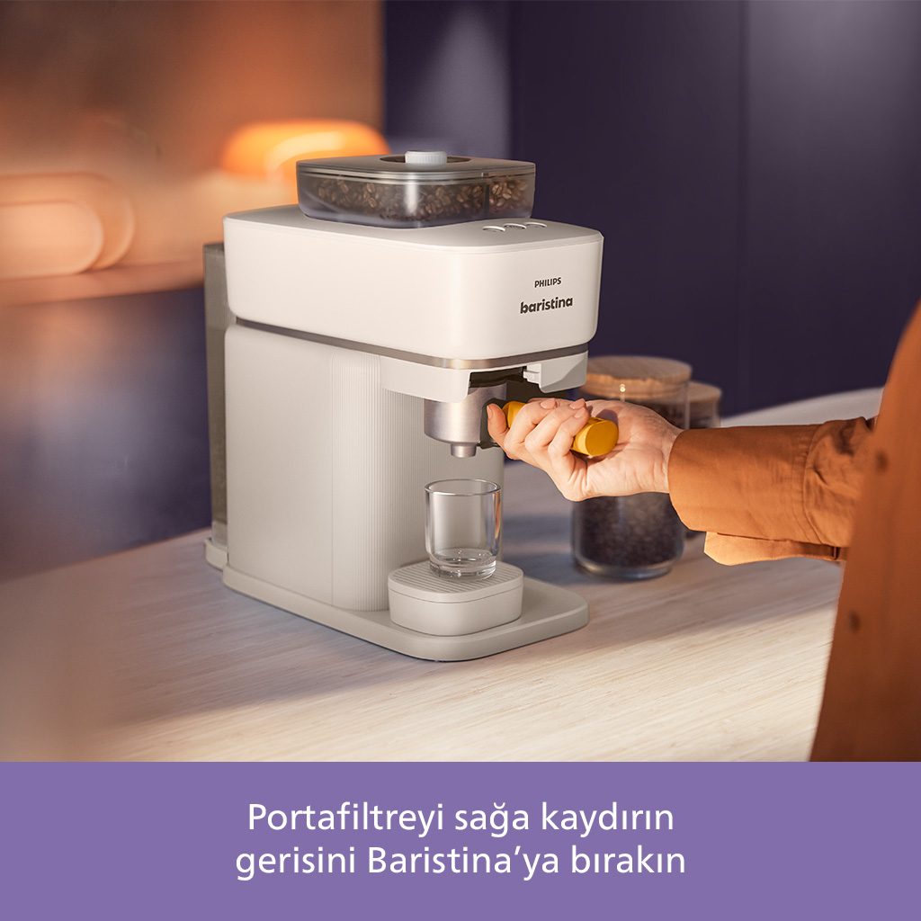 Beyaz bir Philips Baristina kahve makinesi, portafiltreyi tutan bir el. Üst kapta kahve çekirdekleri görülüyor.